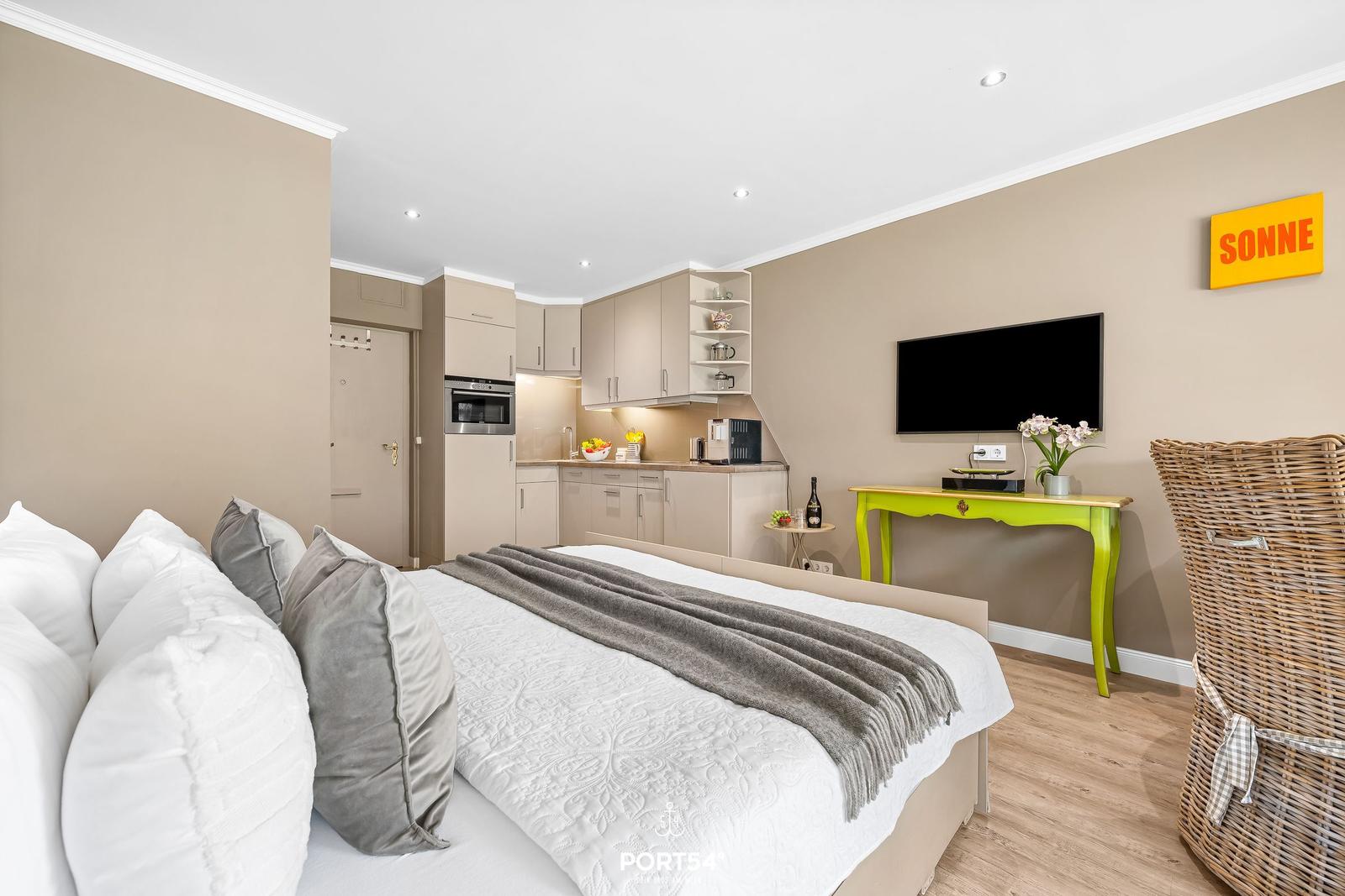 Bedroom with bed, kitchenette, and TV. Wall art with sun.