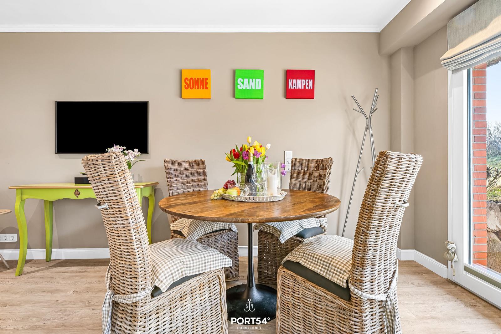 Round table with four chairs, wall art and TV. Window with view outside.