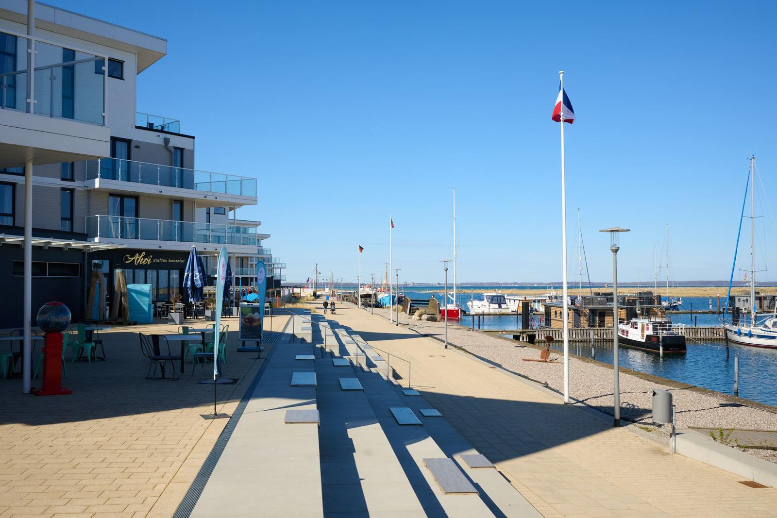 Promenade am Hafen mit Booten und modernem Gebäude.