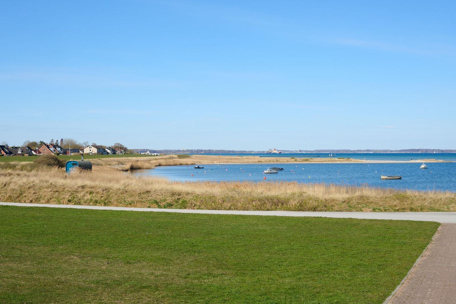 Grüner Rasenweg führt zum Ufer mit Booten und Blick auf das Meer.