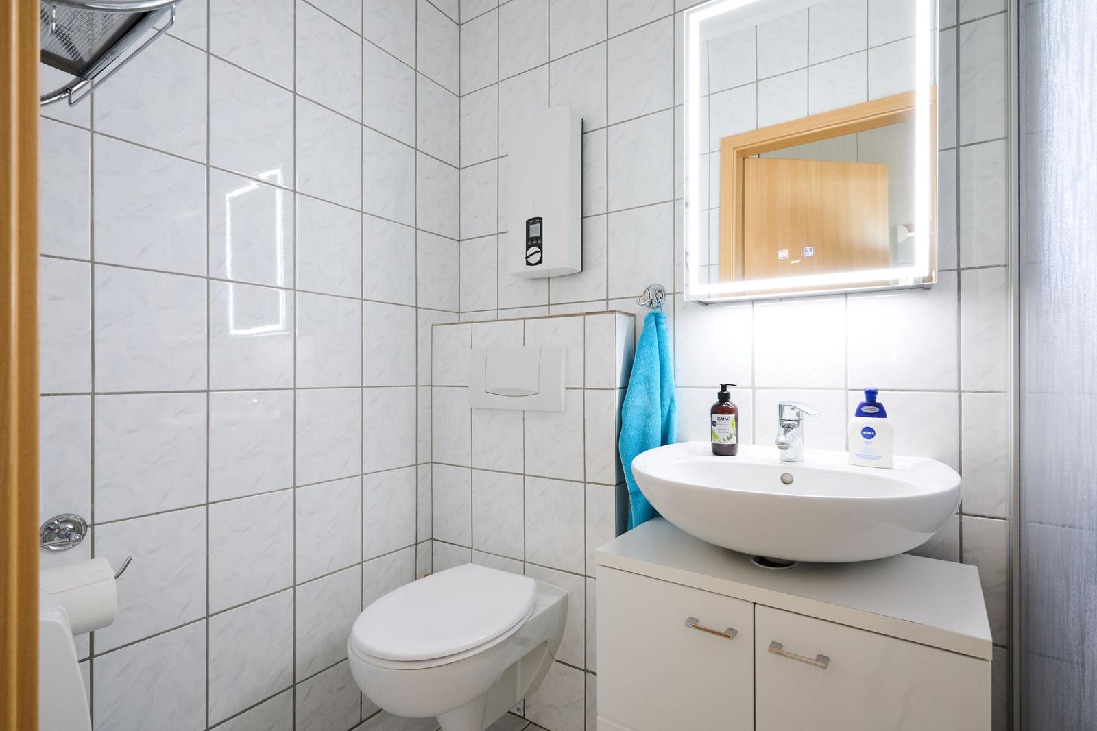 Badezimmer mit Toilette, Waschbecken und beleuchtetem Spiegel.