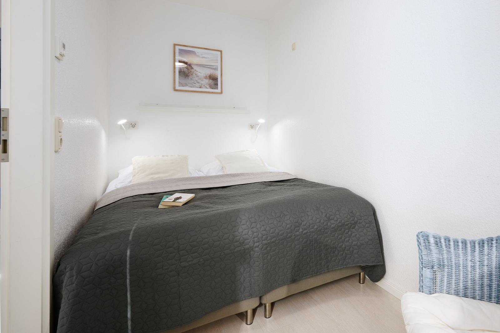 Schlafzimmer mit Bett, Wandbild und Stehlampe. Holzfußboden und weißer Wand.