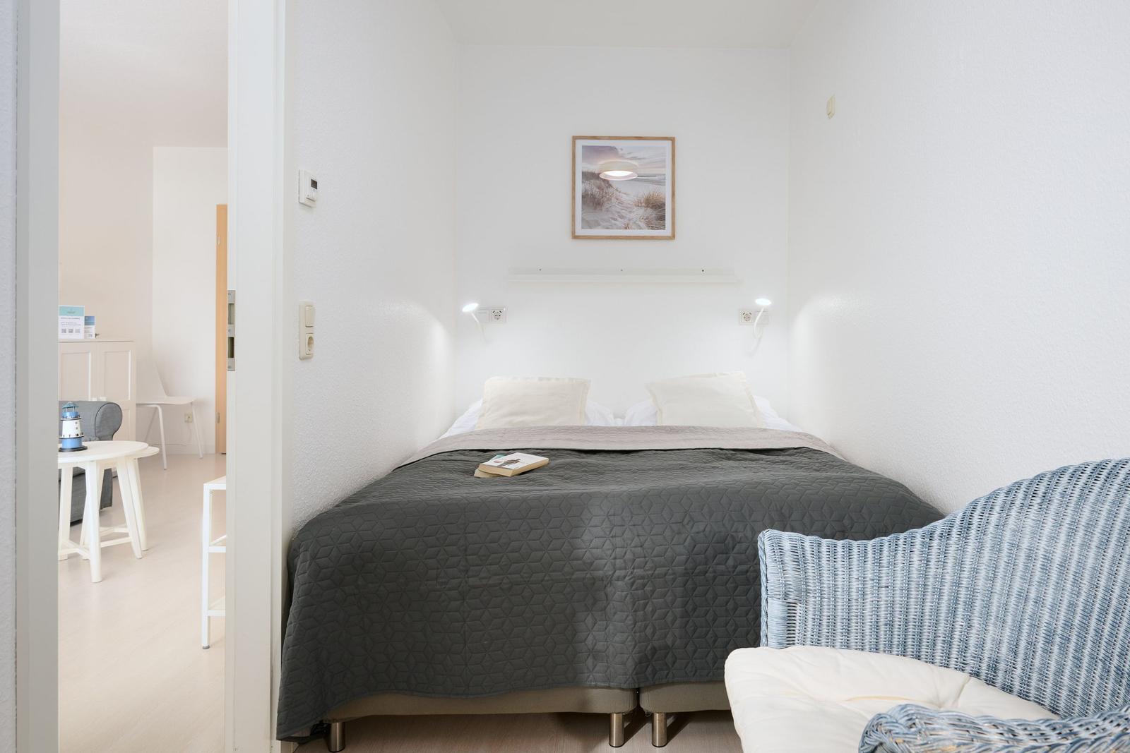 Schlafzimmer mit Bett, Wandbild und Sessel. Blick in angrenzenden Raum.