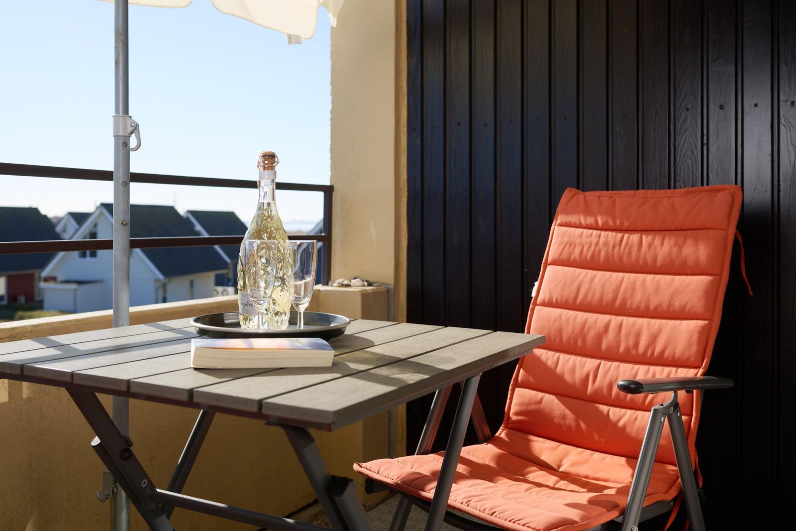 Terrasse mit Tisch, orangefarbener Stuhl und Flasche Champagner.