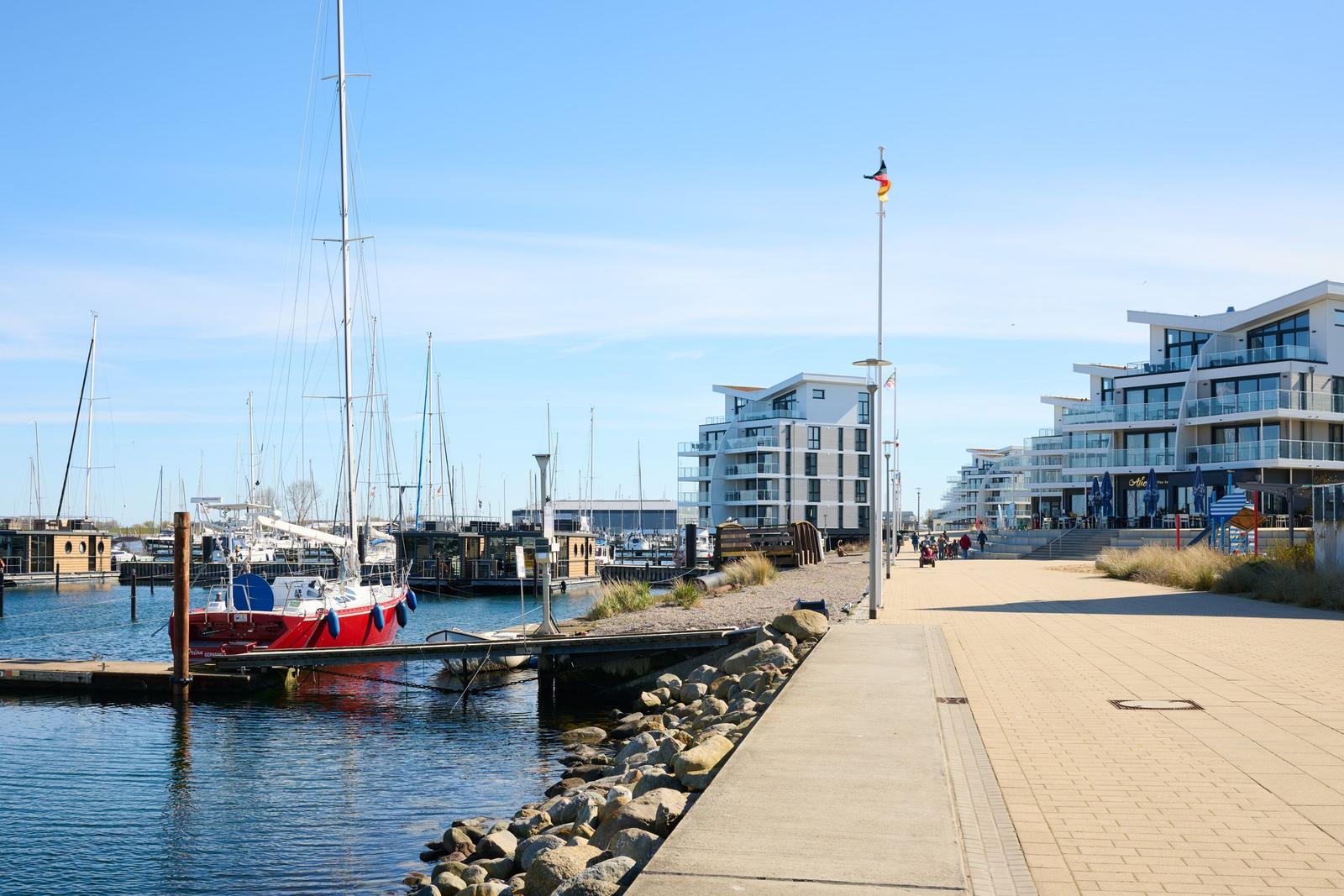 Hafenpromenade mit Segelbooten und modernen Gebäuden am Wasser.