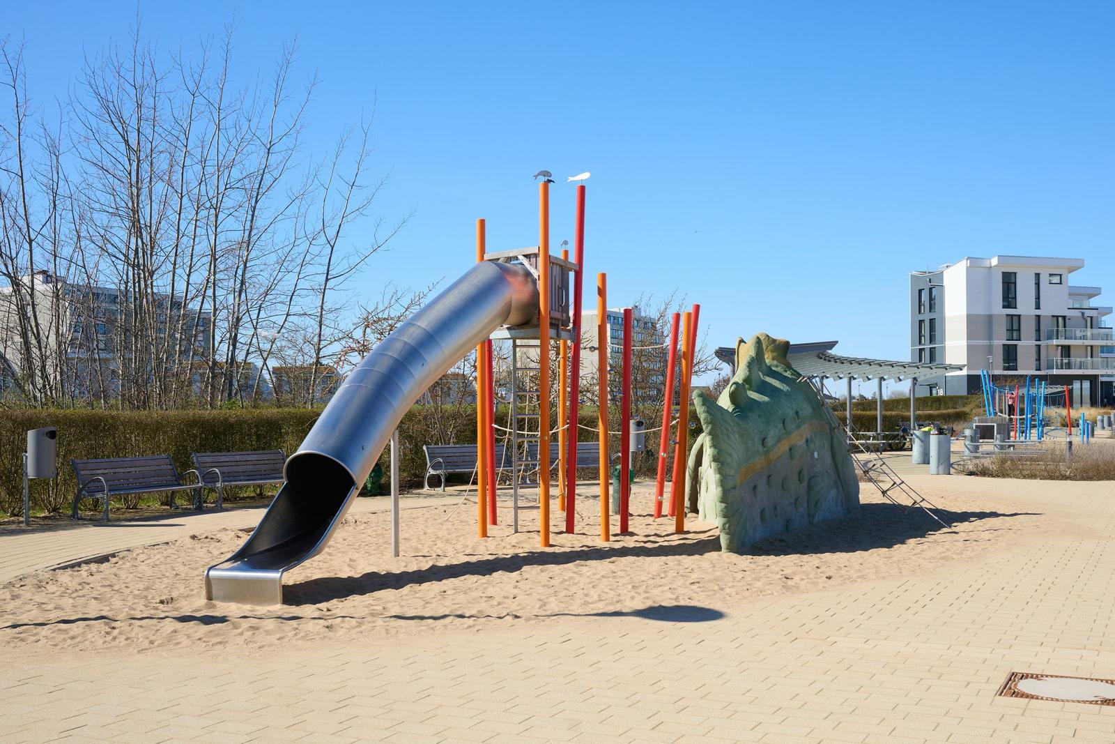 Kinder-Spielplatz mit Rutsche und Klettergerüst auf Sandfläche.