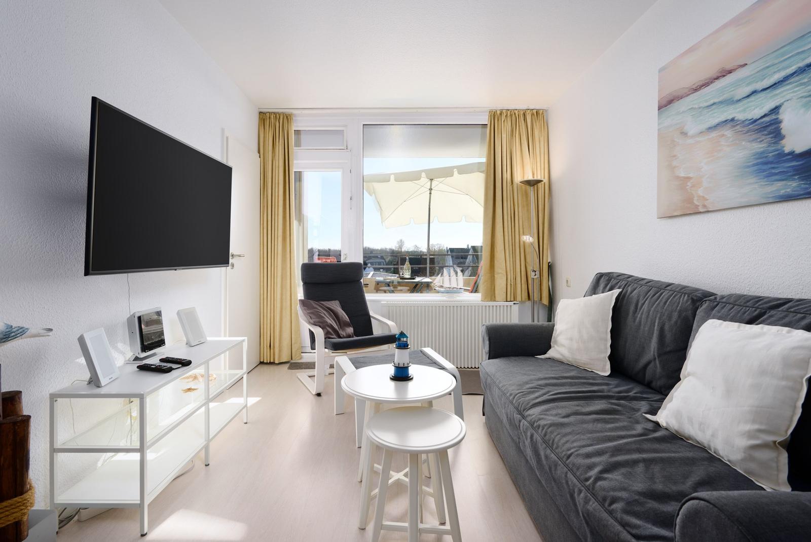 Wohnzimmer mit Sofa, Fernseher und Balkonblick