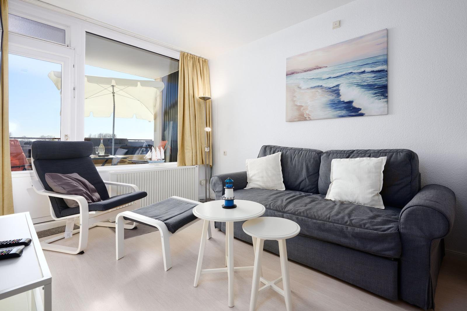 Wohnzimmer mit Sofa, Sitzbank und Tisch. Fenster mit Blick auf Balkon.