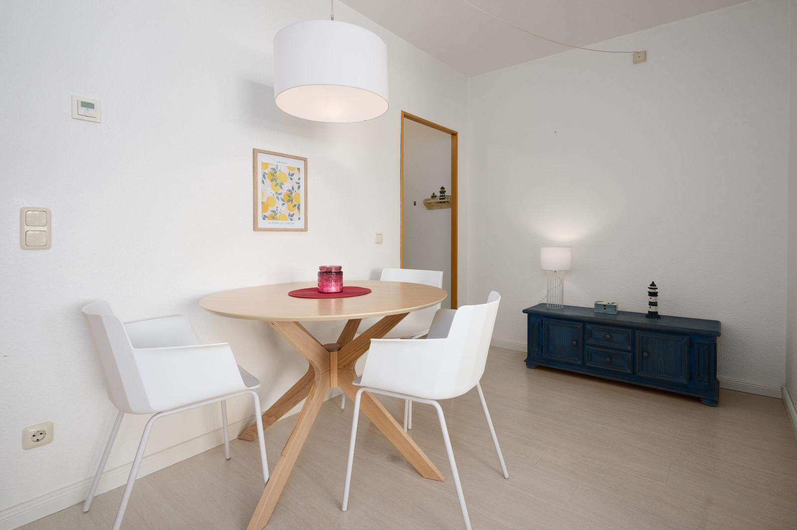 Rundes Esszimmer mit weißer Tischplatte und vier Stühlen. Dunkelblauer Schrank und Lampe.