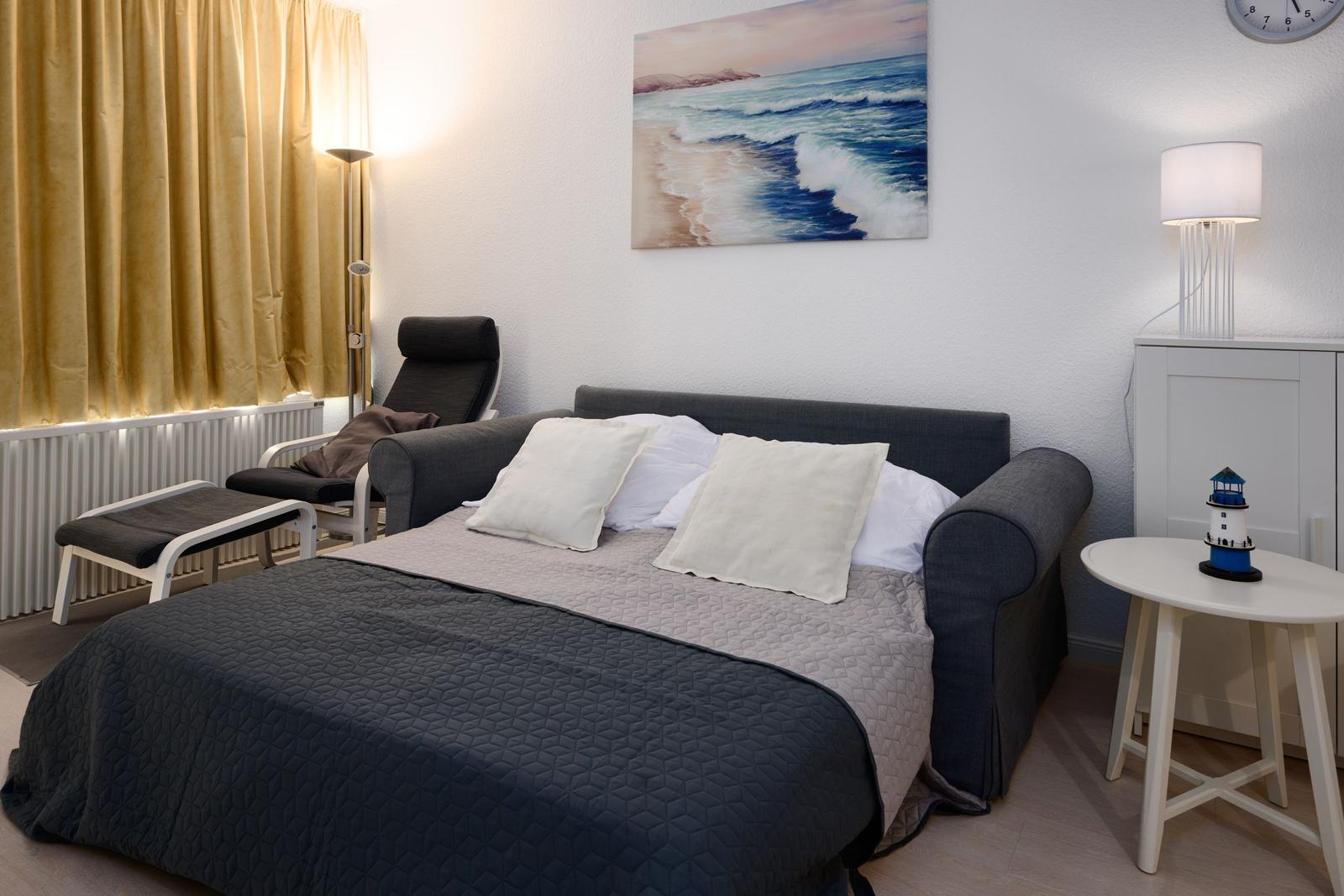 Schlafzimmer mit Bett, Stuhl, Wandbild und Nachttisch.