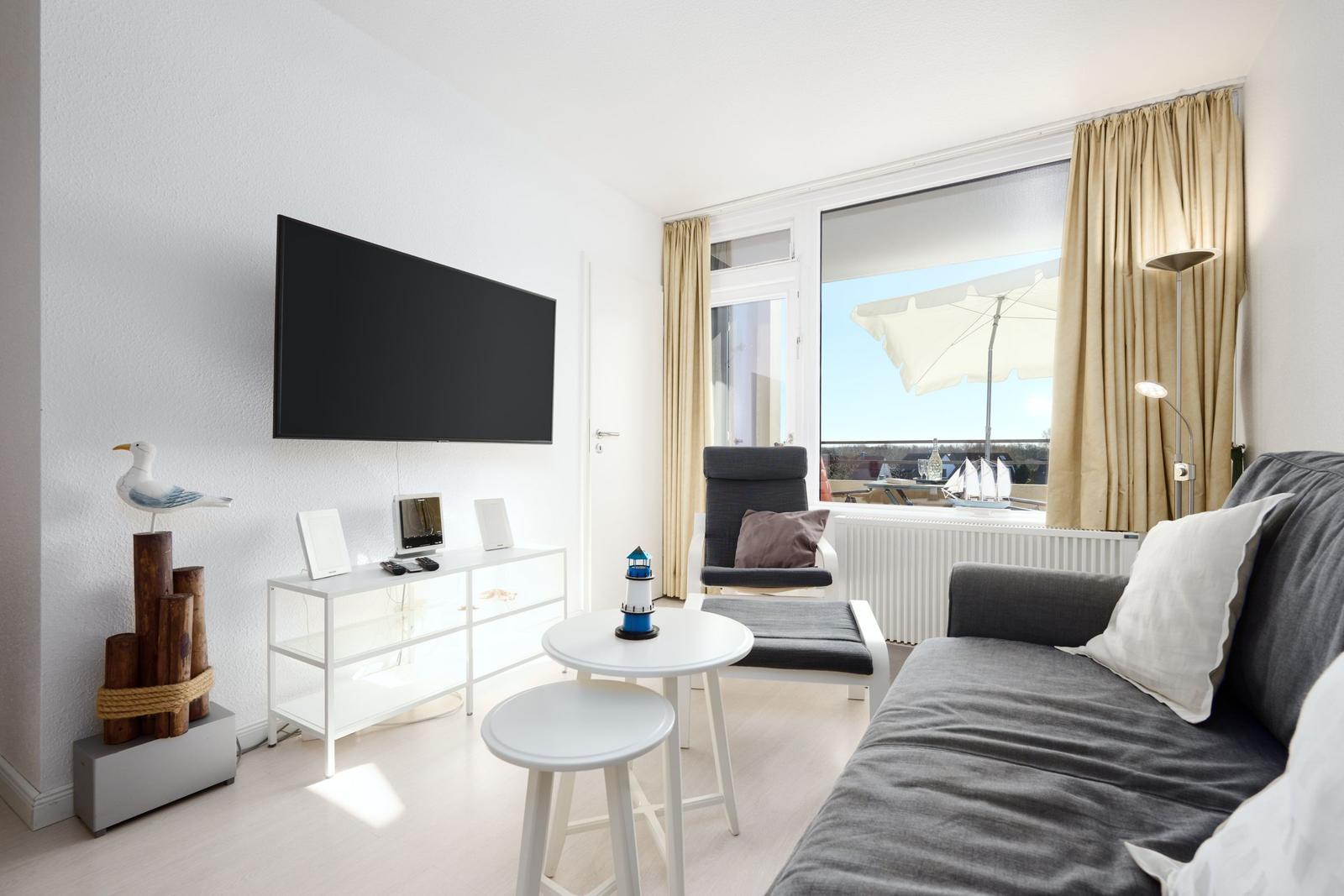 Wohnzimmer mit Sofa, Fernseher und Balkonansicht.