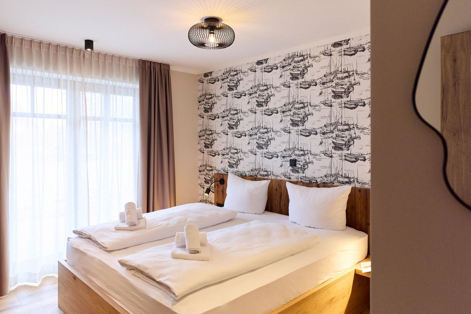 Schlafzimmer mit Bett, Fenster und Wand mit Booten-Motiv.