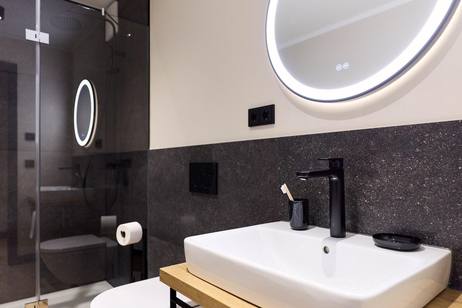 Bad mit Waschbecken, Spiegel und Dusche. Schwarze Wand und Holzunterschrank.