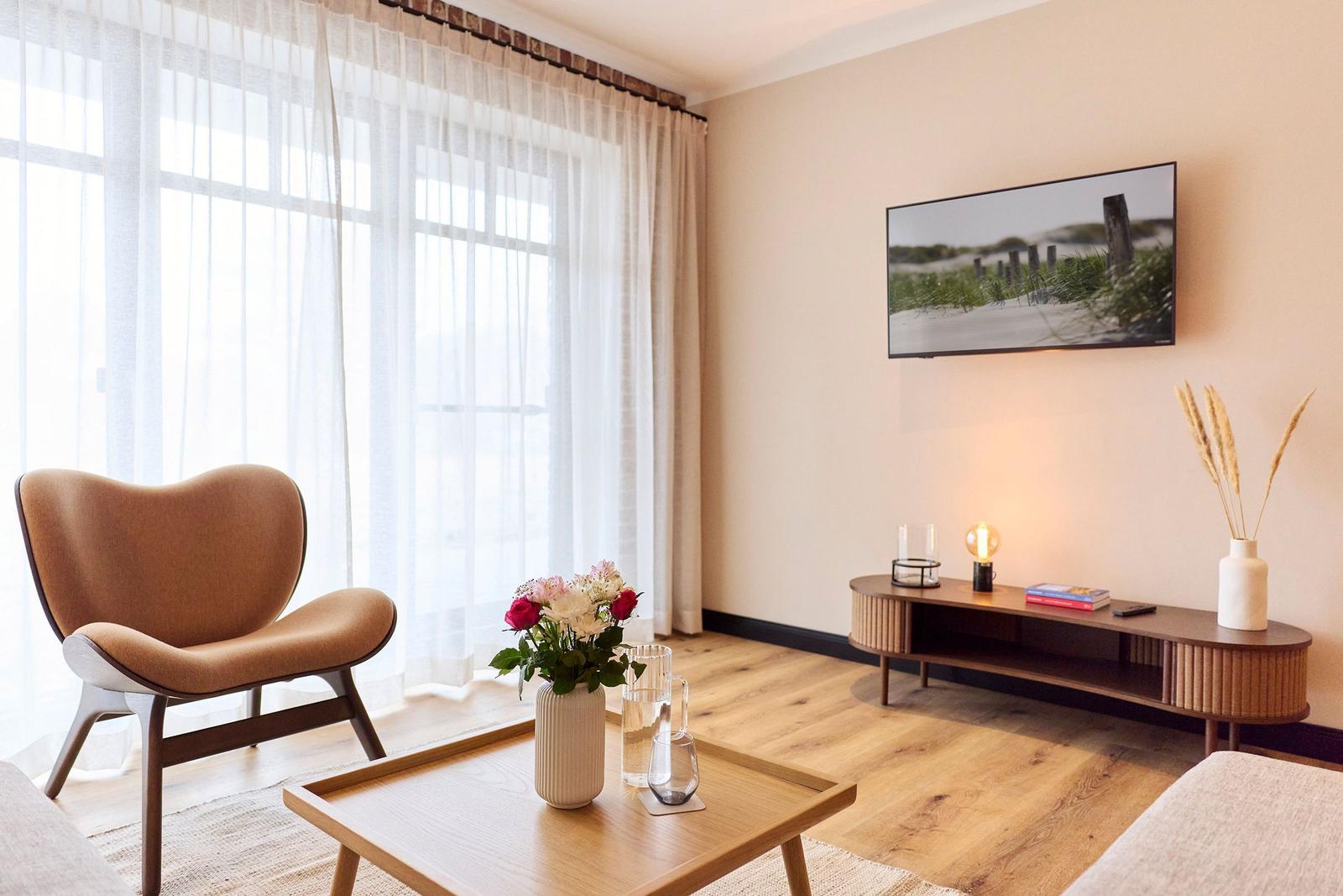 Wohnzimmer mit Sessel, Couchtisch und Fernseher an der Wand.