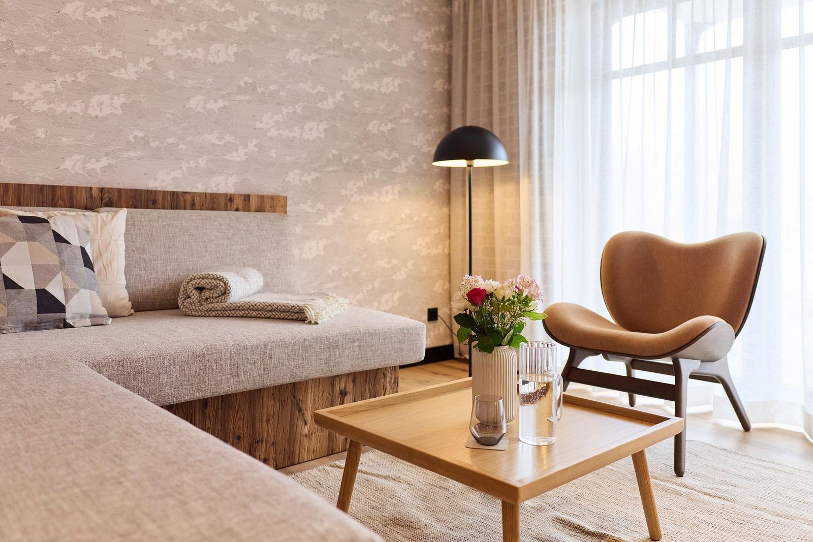 Ein Raum mit Sofa, Sessel, Tisch und Blumen vor einem Fenster.