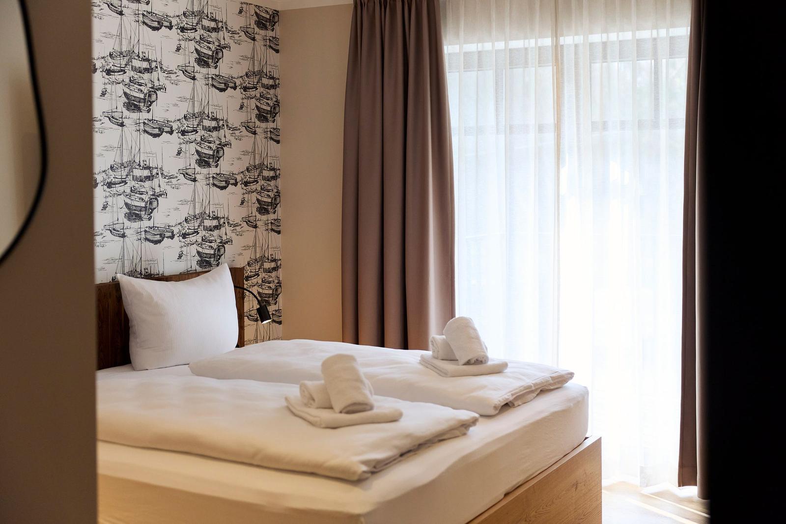 Schlafzimmer mit Bett, weißen Handtüchern und Wandtapete mit Bootsmotiv.
