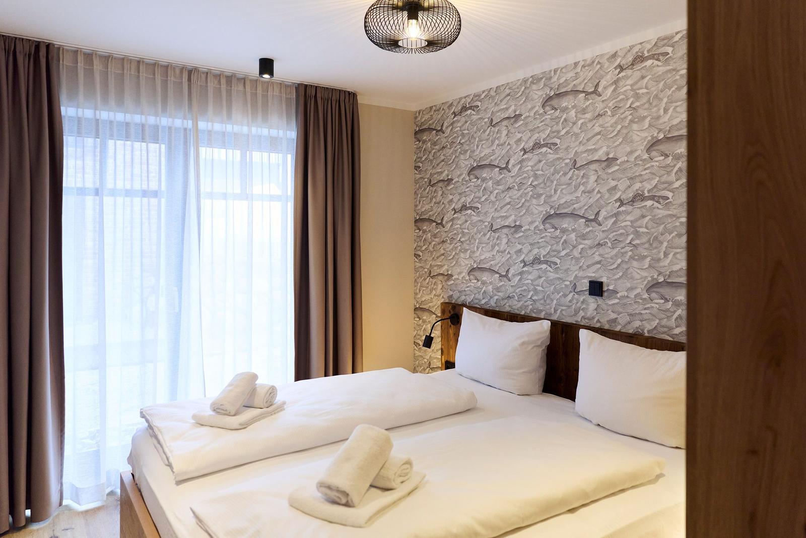 Schlafzimmer mit Bett, Wandtapete mit Fischmotiv und Fenster mit Vorhängen.