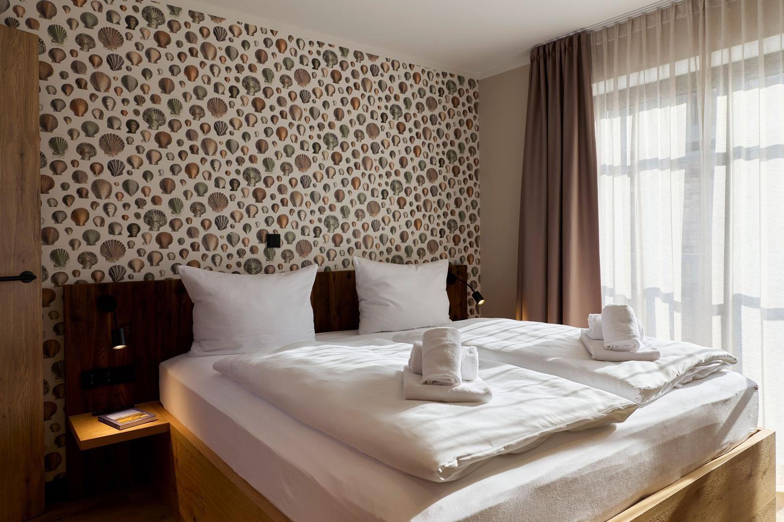 Schlafzimmer mit Bett, weißen Laken und Schalentapete an der Wand.