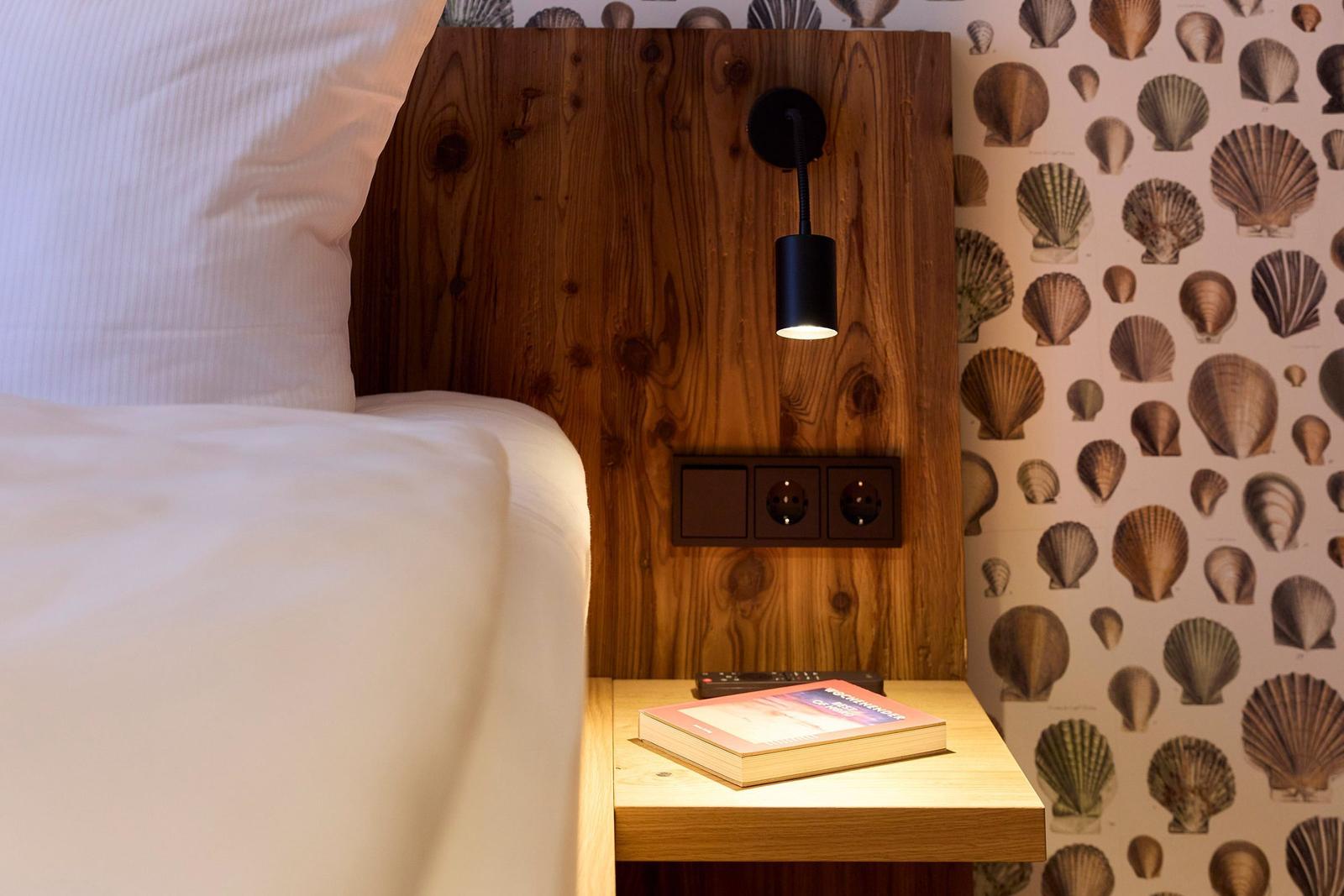 Schlafzimmer mit Holz-Kopfteil, Schneckenaufkleberwand und Nachttisch mit Buch.