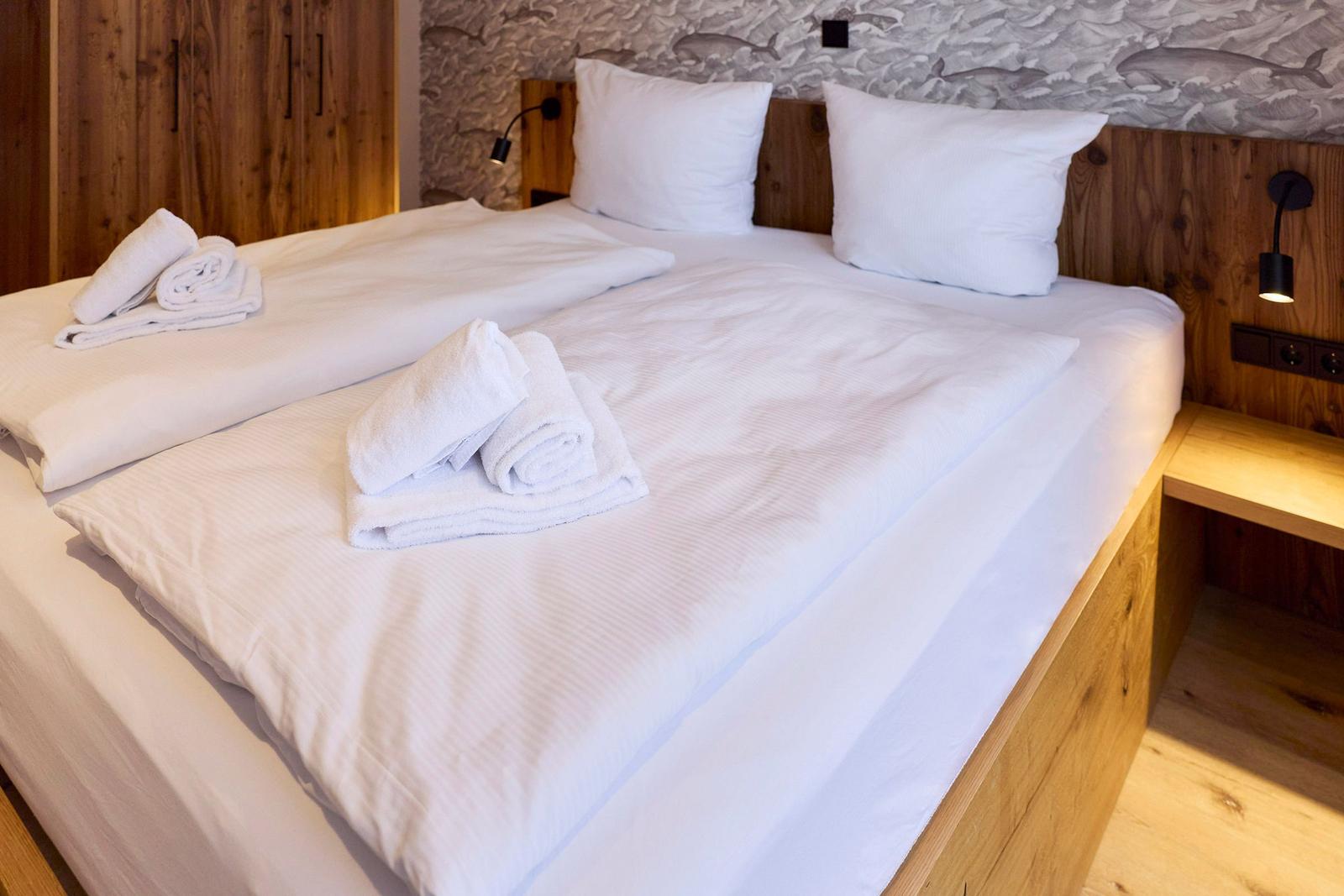 Doppelbett mit weißen Laken und Handtüchern, Holzwand und Fischmotivtapete.