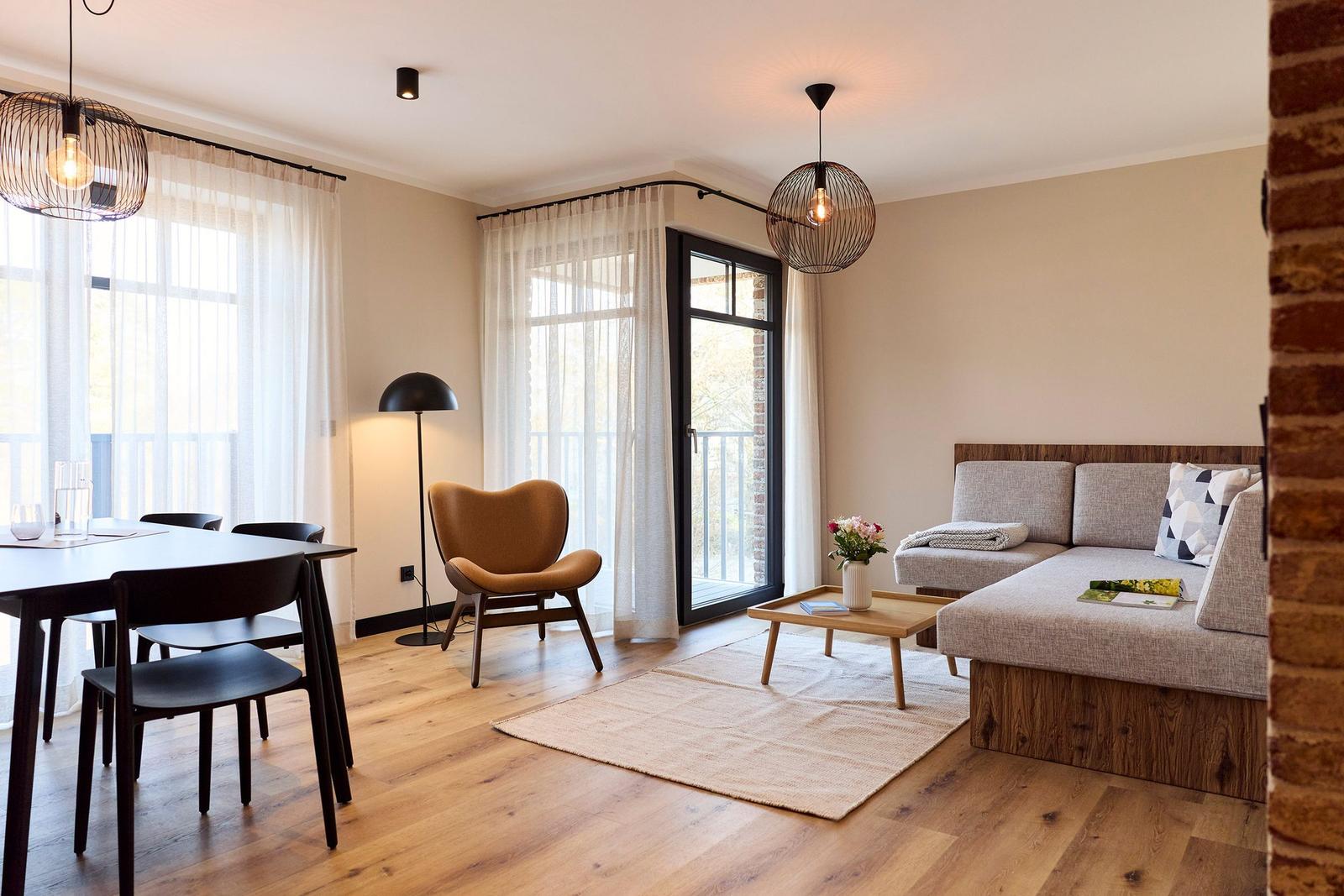 Wohn- und Essbereich mit Sofa, Tisch und Stühlen sowie Fenstern und Balkontür.