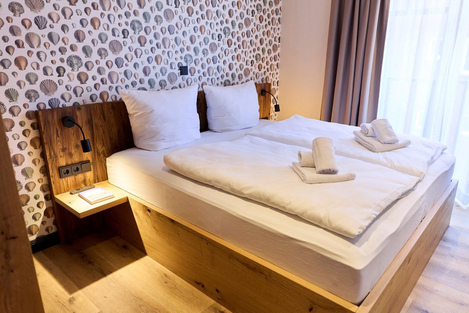 Ein Bett mit weißer Bettwäsche und Handtüchern. Wand mit Muschel-Motiv und Holzbett.