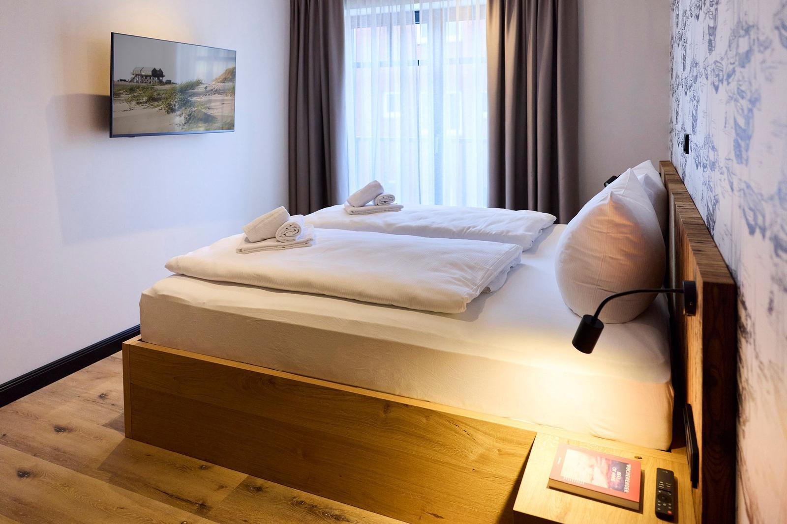 Schlafzimmer mit Bett, Fernseher und Fenster mit Vorhängen.