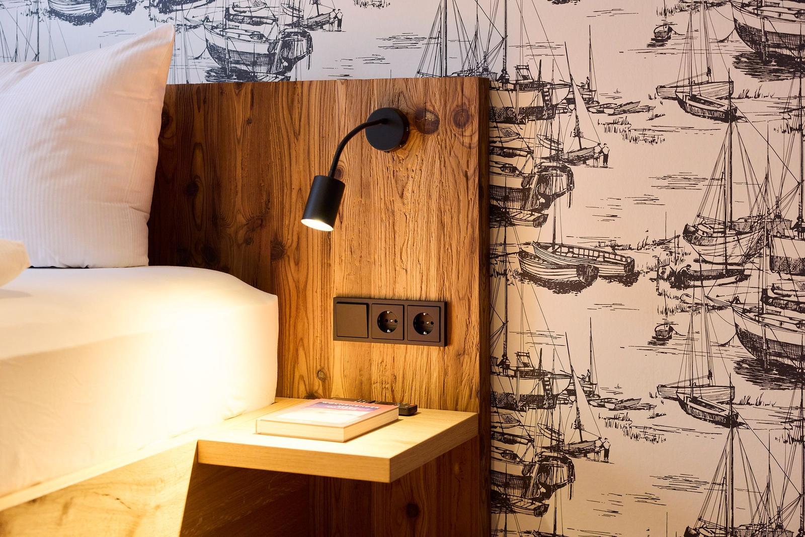 Schlafzimmer mit Holzkopfteil, Wandbeleuchtung und Segelyacht-Motivtapete.