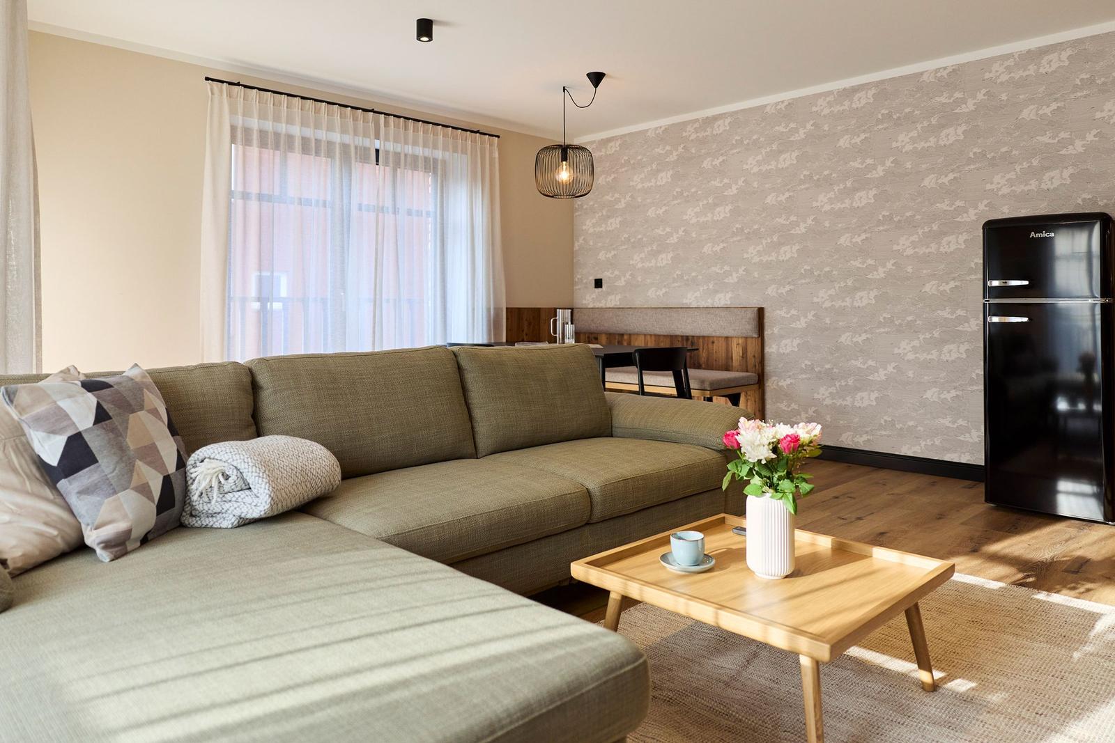 Wohnzimmer mit Sofa, Couchtisch, Kühlschrank und Fenster