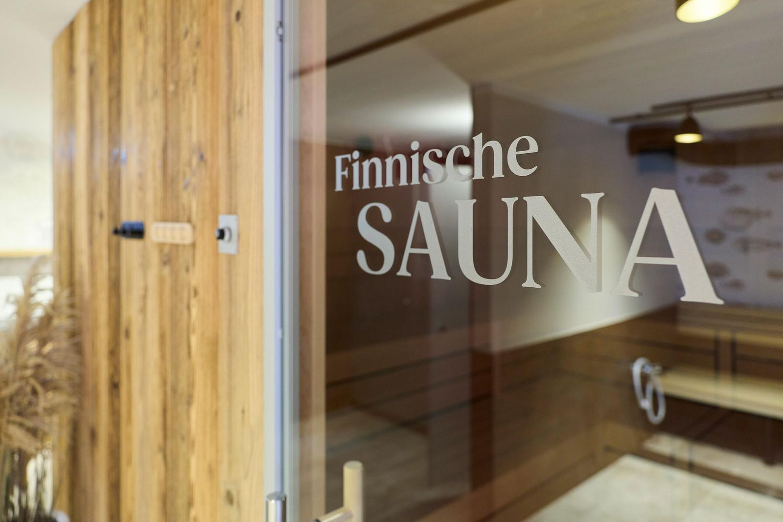 Finnische Sauna mit Holzbank und Glasfront. Tür mit Schriftzug.