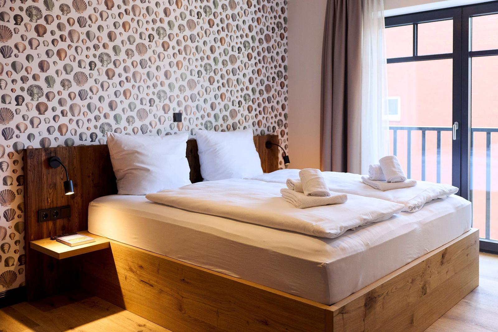 Ein Bett mit weißen Laken und Handtüchern vor einem Fenster mit Balkon und Muschel壁纸.