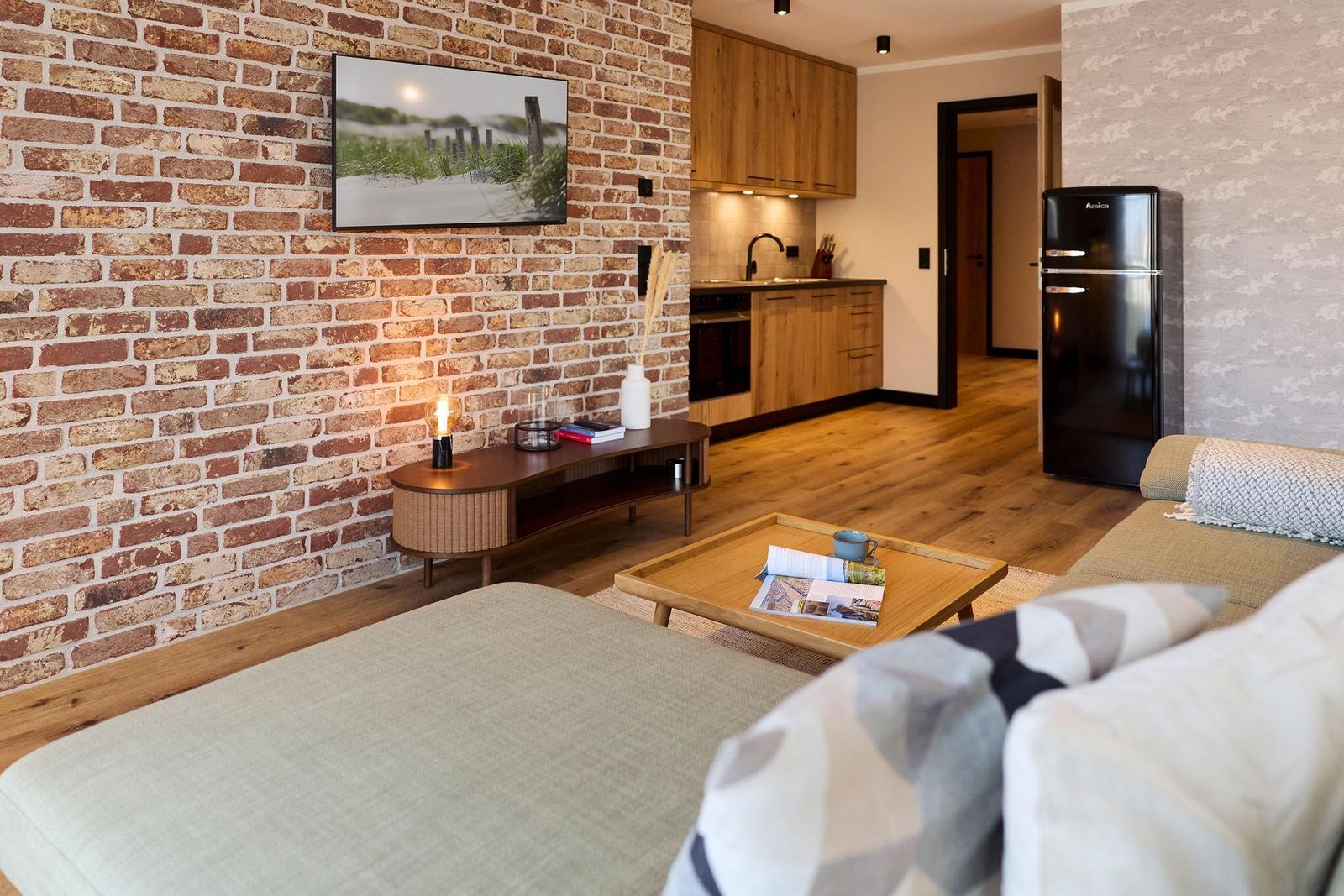 Wohnbereich mit Steinwand, Sofa, Couchtisch und Küchenbereich mit Holzmöbeln.