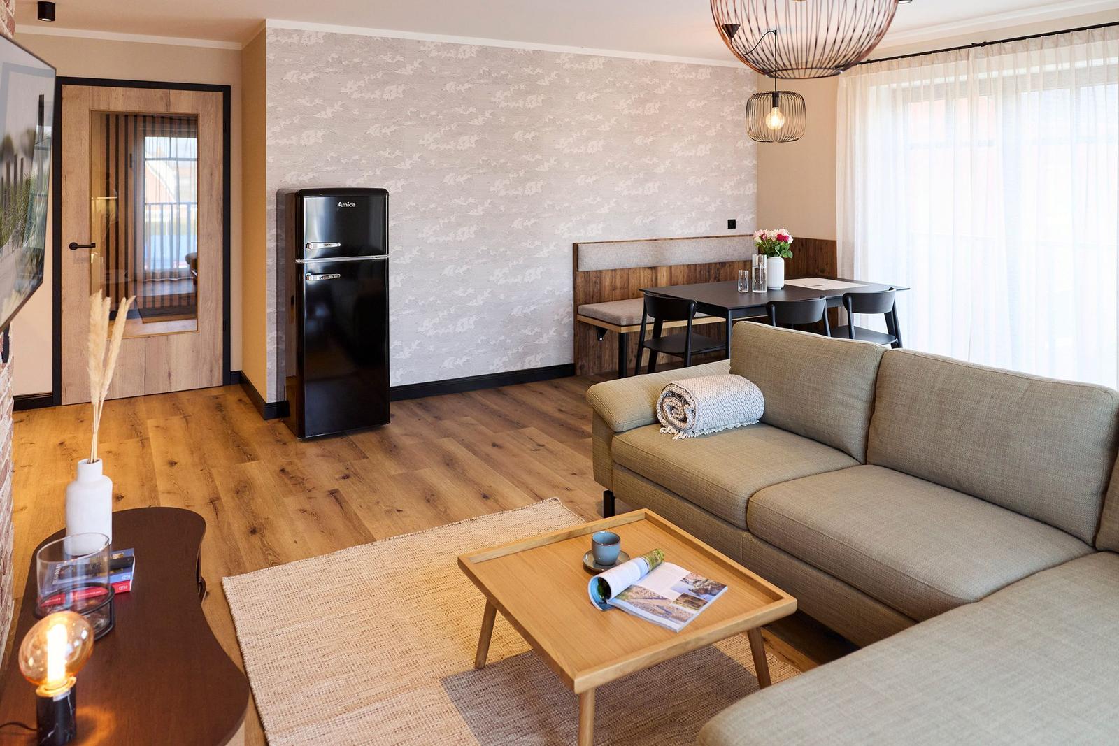 Wohnzimmer mit Sofa, Esstisch, Kühlschrank und Holzboden.