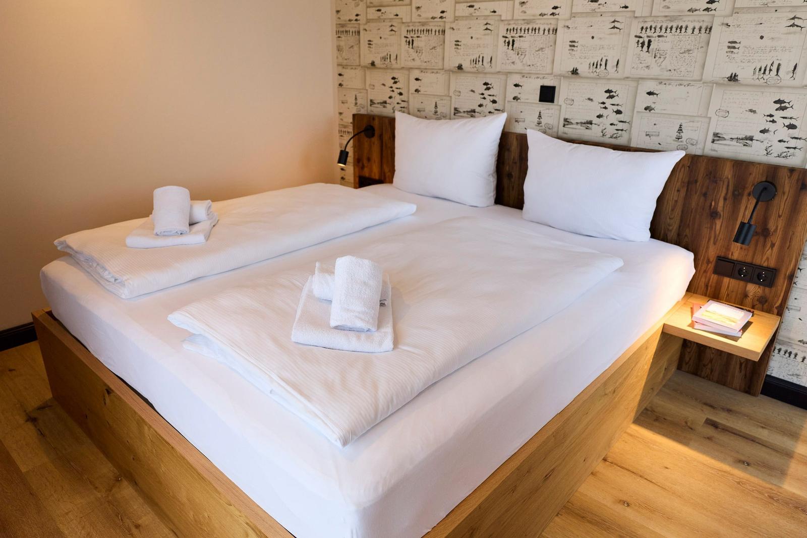 Ein Bett mit weißen Laken und Handtüchern, Holzrahmen und Wand mit Zeichnungen.