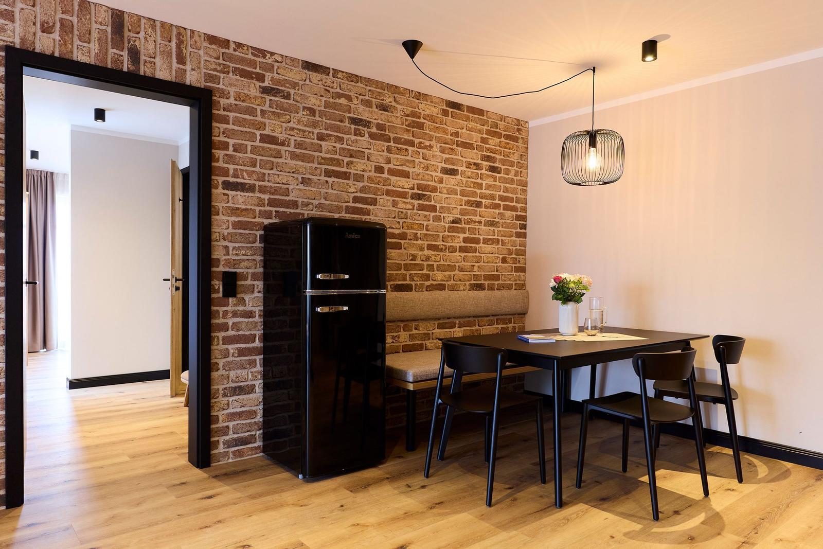Essbereich mit Tisch, Stühlen und Kühlschrank an Backsteinwand.
