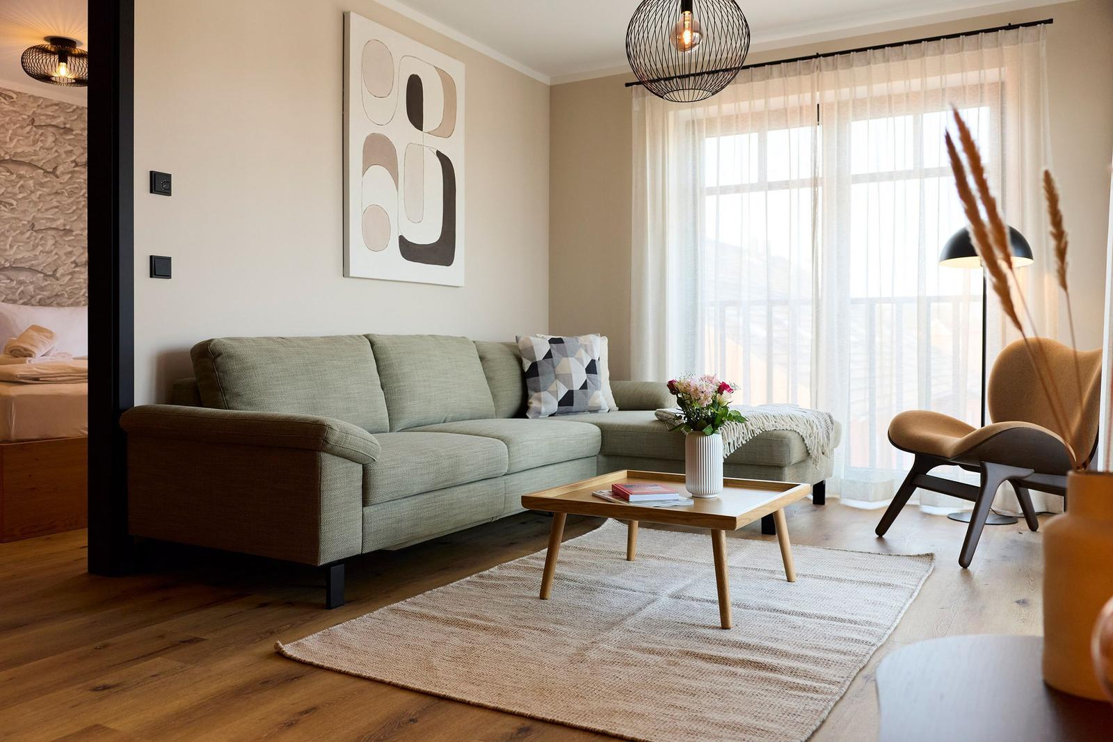 Wohnzimmer mit Sofa, Couchtisch und Sessel. Fenster mit Vorhängen und Wandbild.