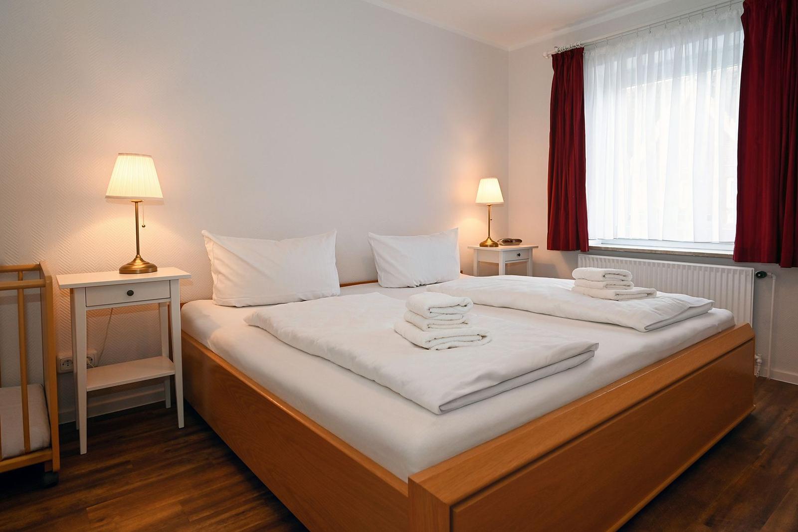 Ein Schlafzimmer mit Doppelbett, zwei Nachttischen und roten Vorhängen an einem Fenster.