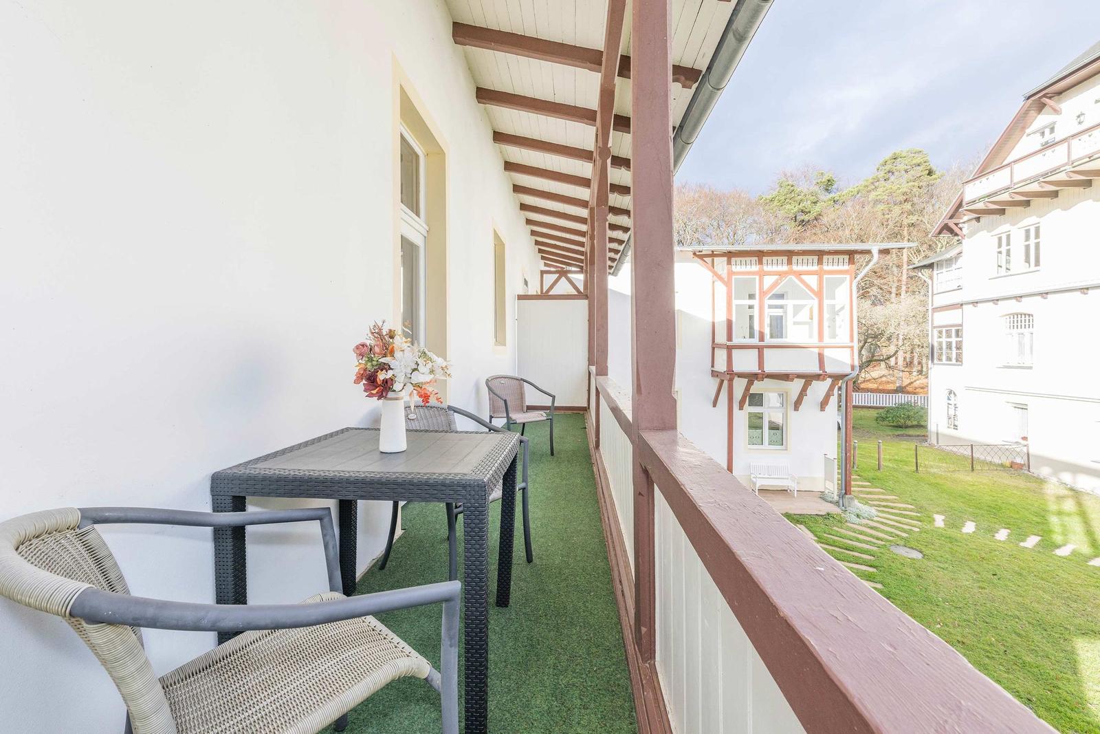 Terrasse mit Tisch, Stühlen und Blumenarrangement. Blick auf Garten und Nebengebäude.