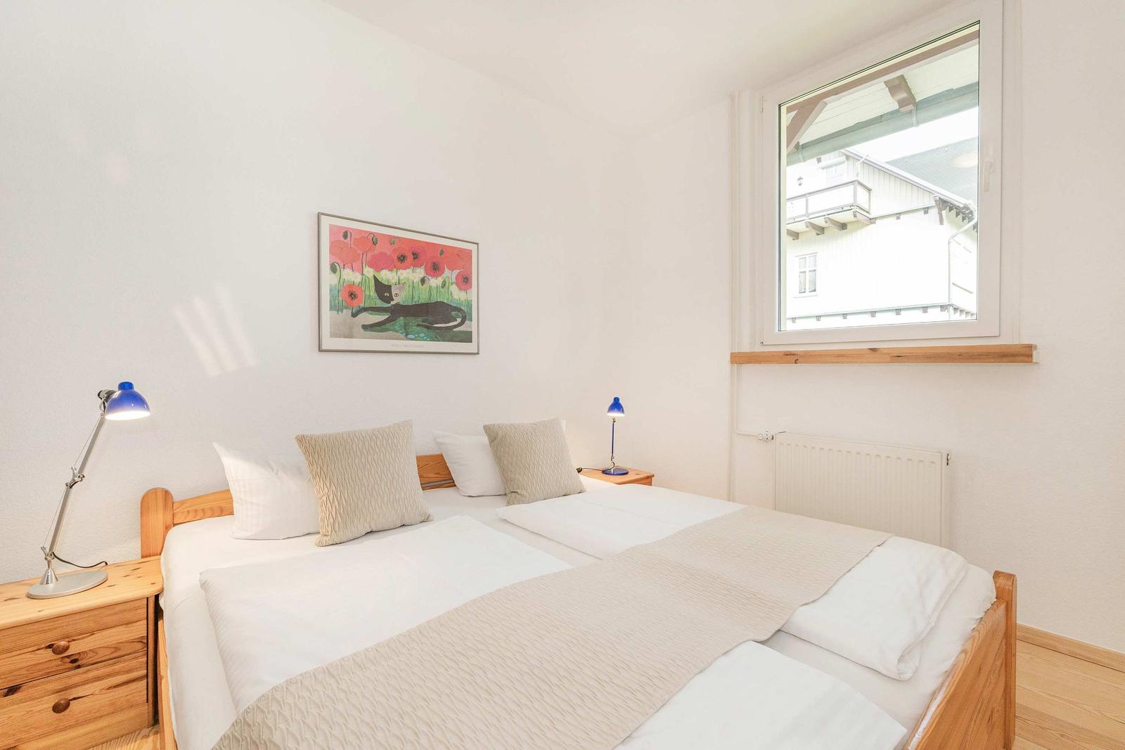 Schlafzimmer mit Doppelbett, zwei Nachttischen und Fensterblick auf Gebäude.