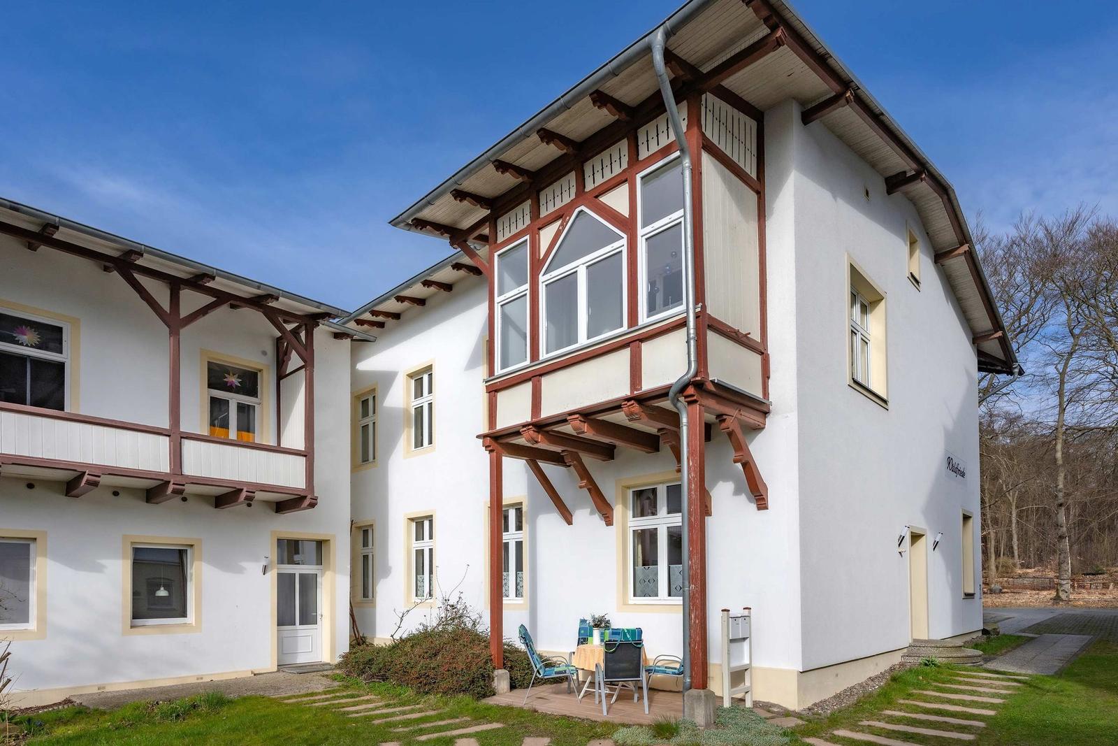 Ein zweistöckiges Haus mit Balkon und Garten. Tische und Stühle stehen draußen.