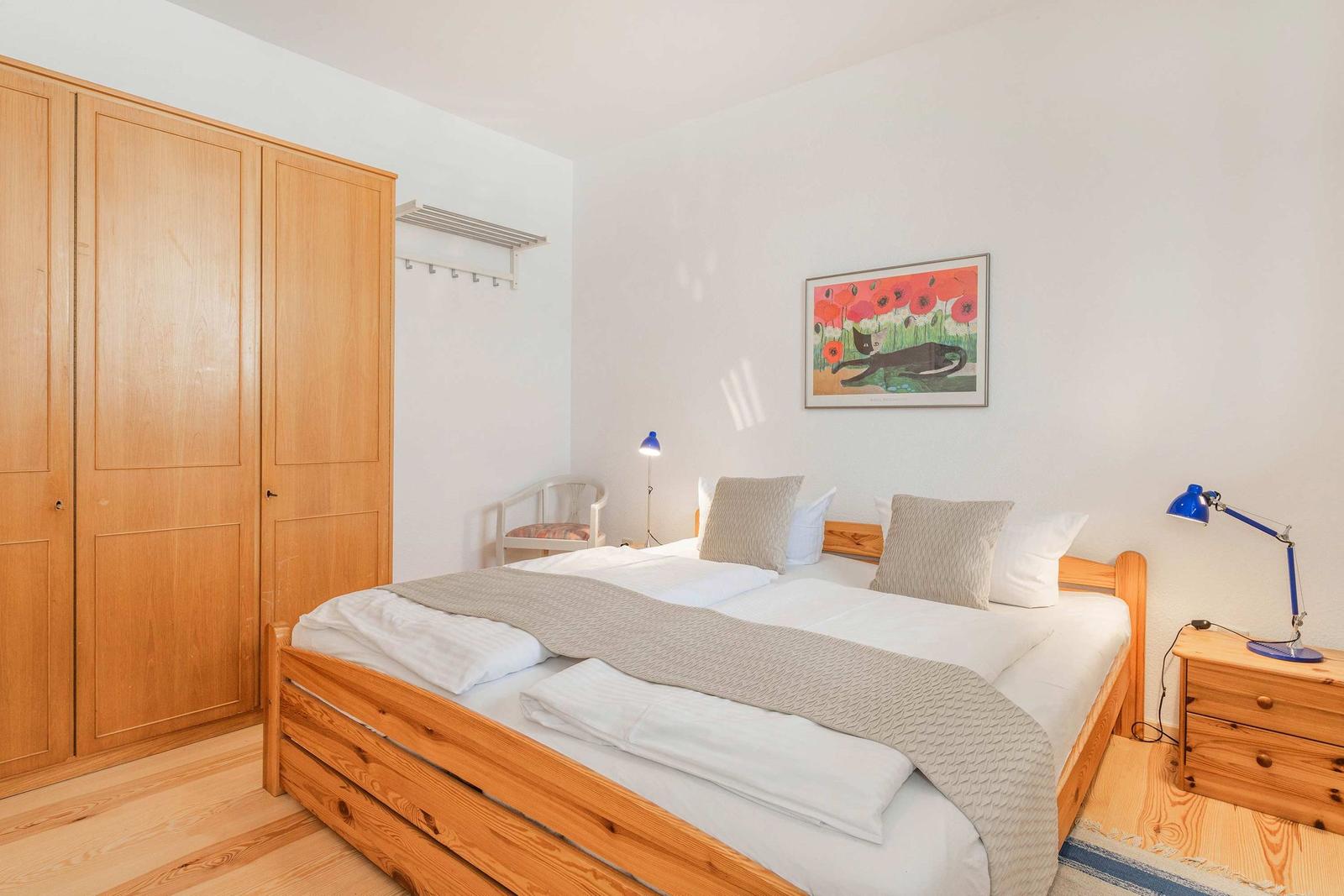 Schlafzimmer mit Holzbett, Kleiderschrank und Wandbild mit Katze.