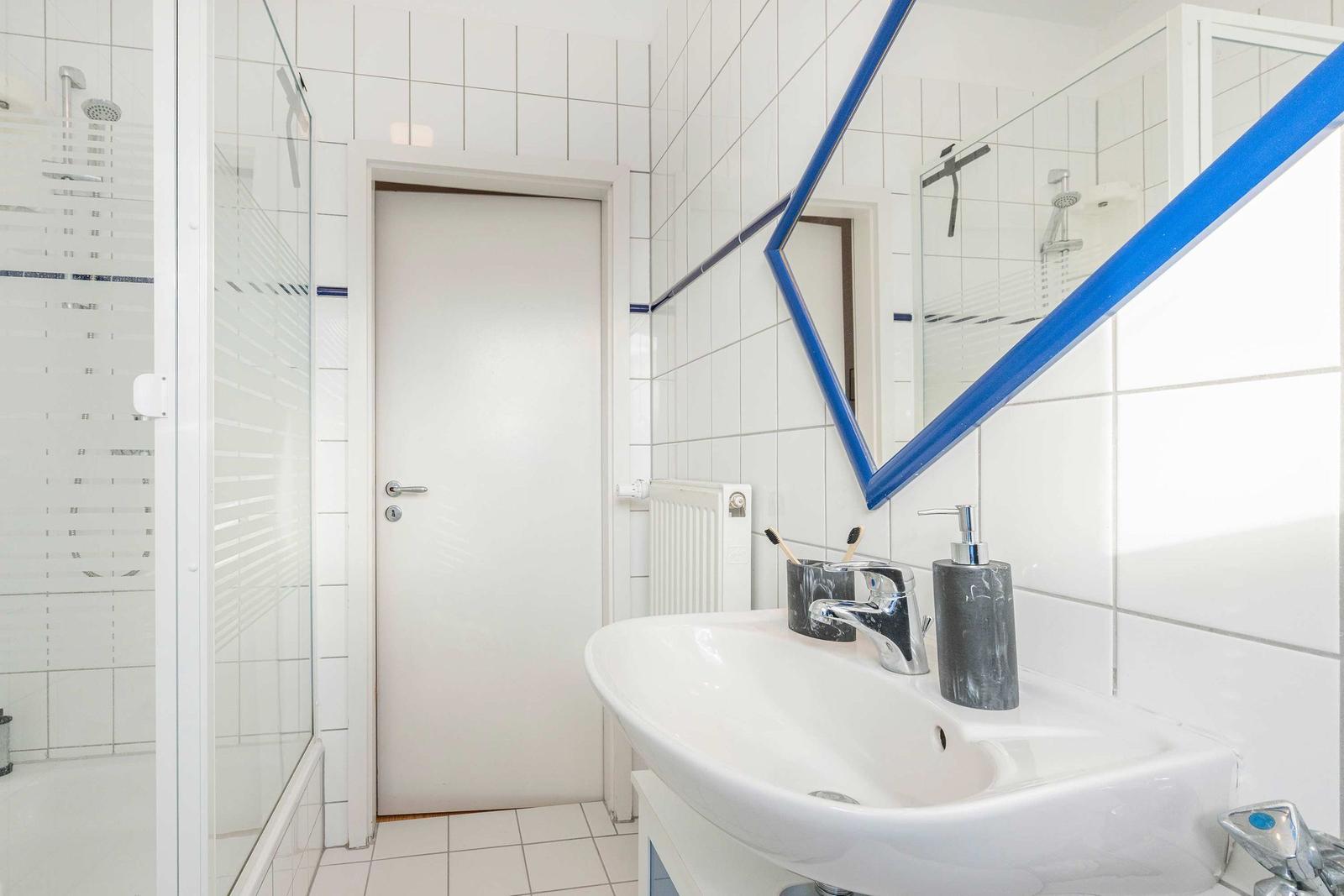 Badezimmer mit Dusche, Waschbecken und Spiegel mit blauem Rahmen.