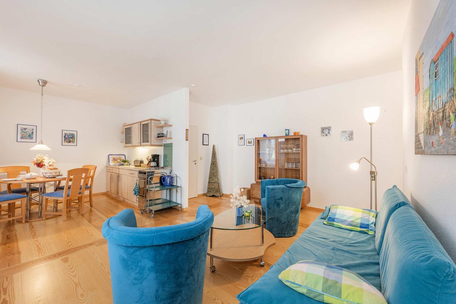 Wohn- und Essbereich mit blauer Couch, Esstisch und Küchenzeile.