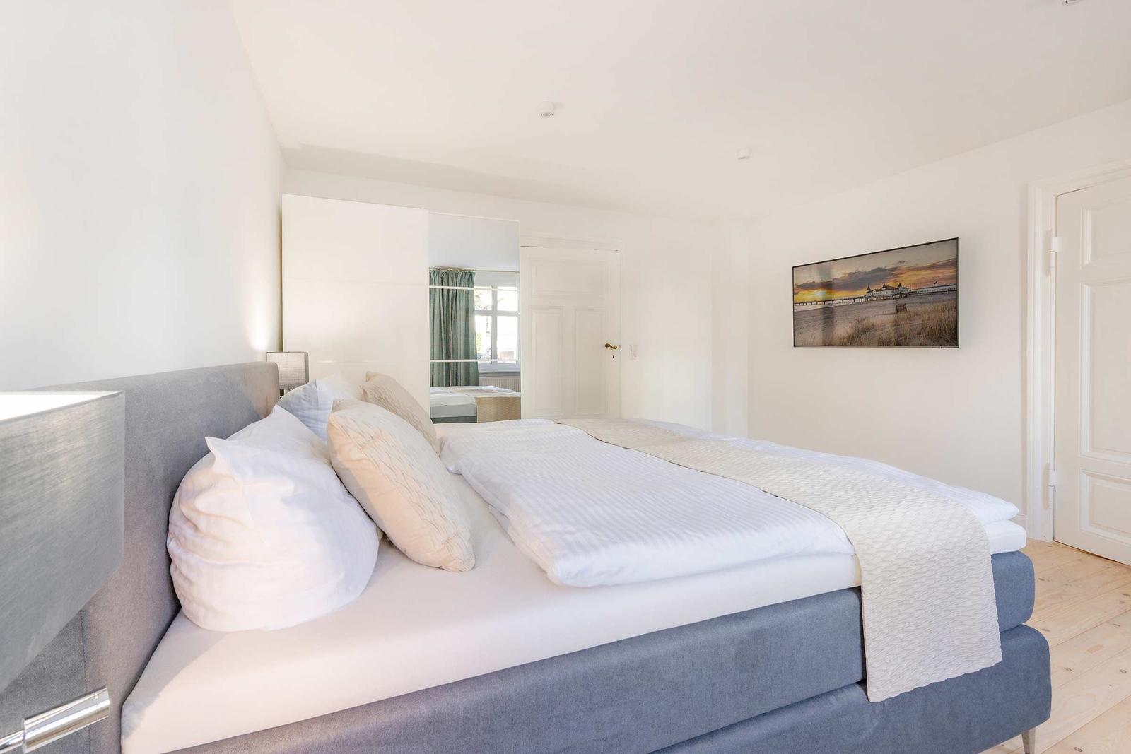 Schlafzimmer mit Bett, Wandbild und Spiegeltüren.
