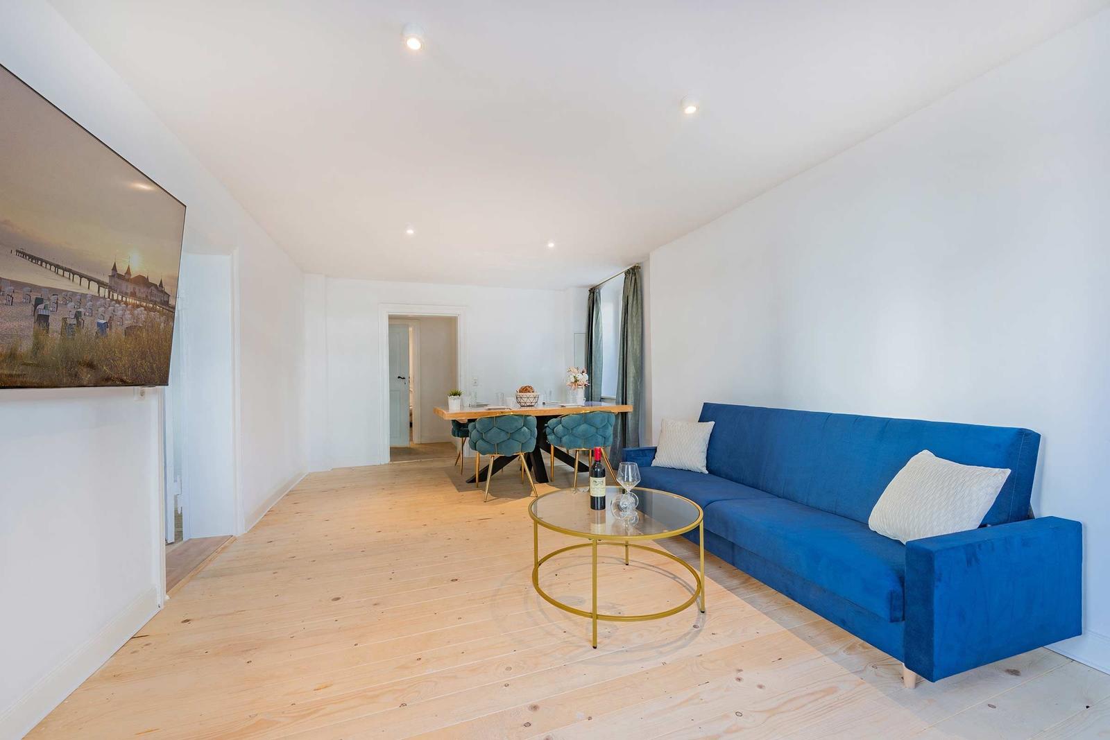 Ein Wohn- und Essbereich mit blauem Sofa, Glas-Tisch und Holzboden.