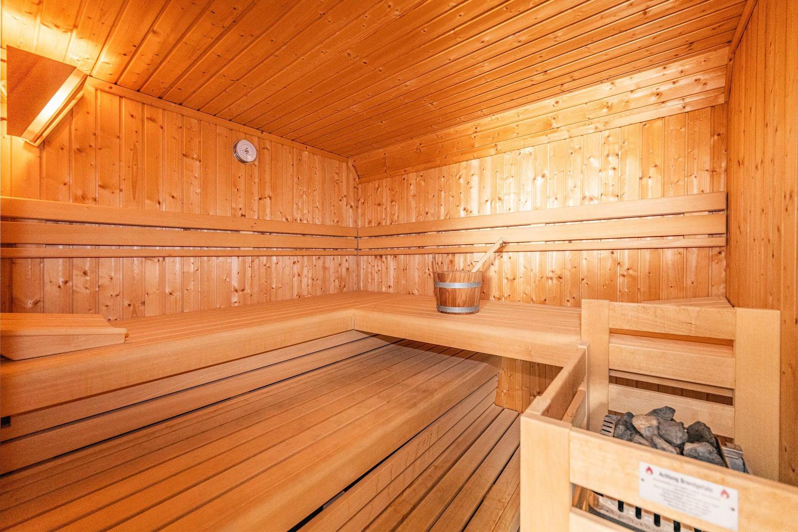 Holzsauna mit mehreren Sitzbänken, Eimer und Steine.