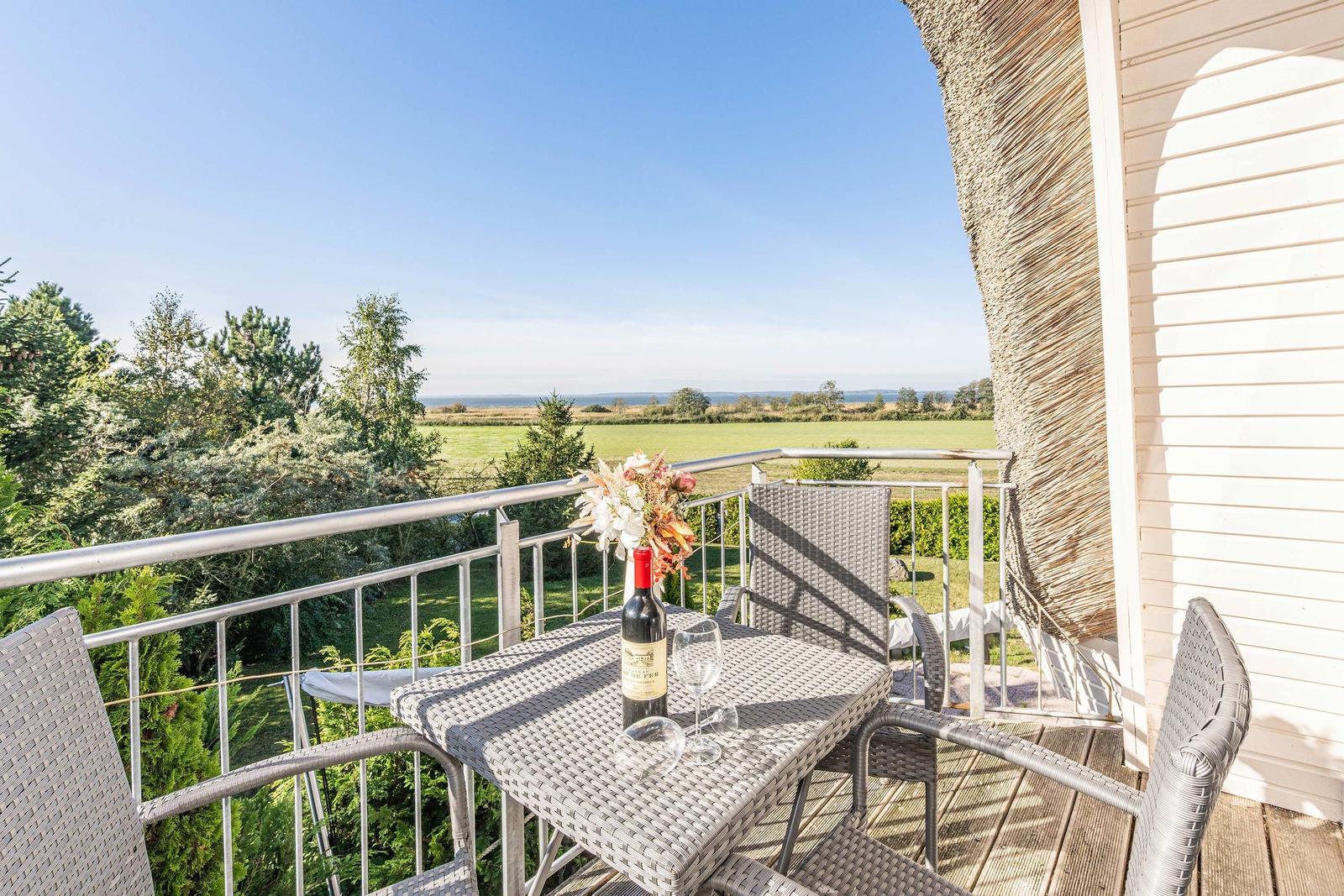 Terrasse mit Tisch, Stühlen und Weinkrug. Blick auf grüne Landschaft und Himmel.