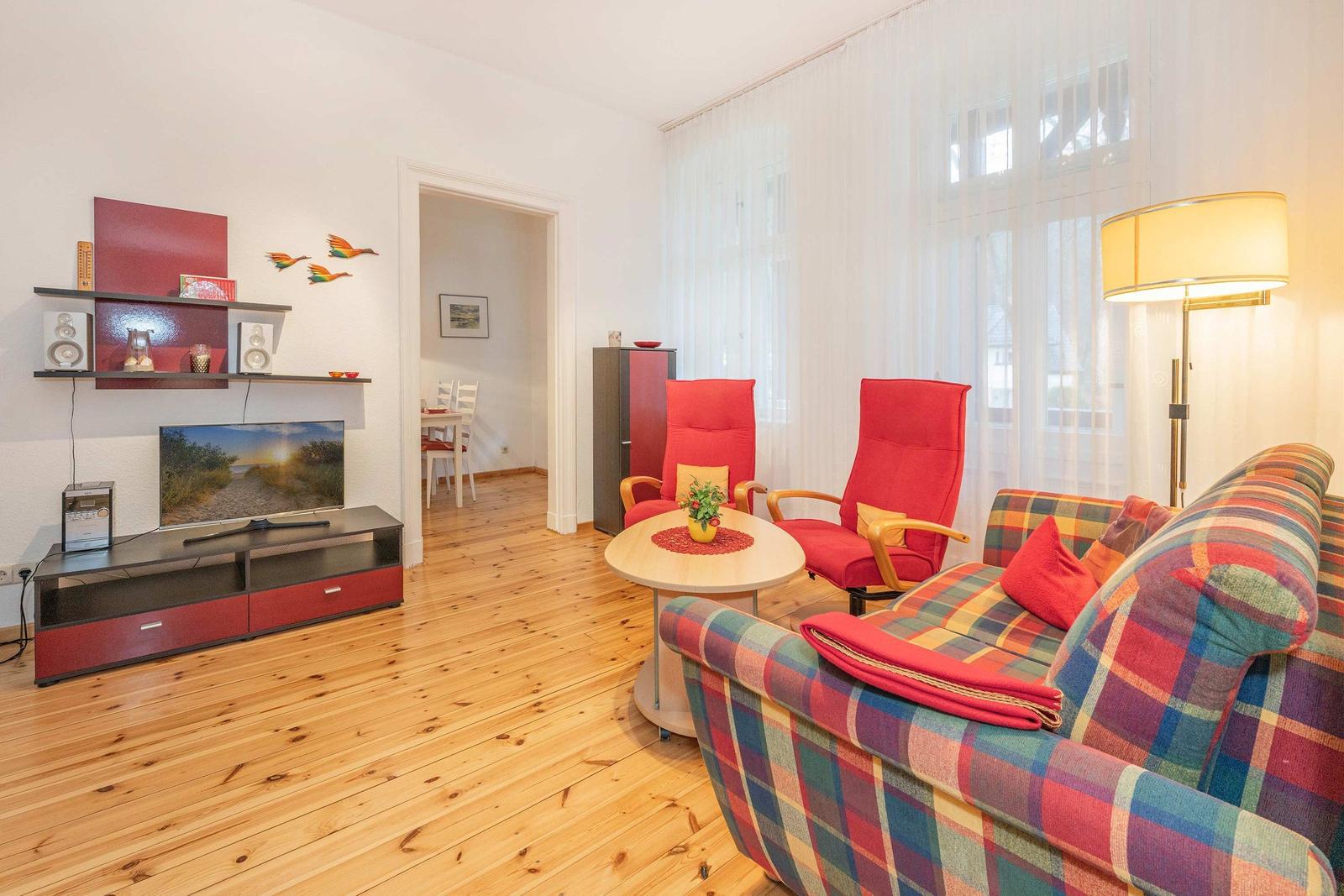 Wohnzimmer mit Sofa, zwei roten Sesseln, Fernseher und Holzboden.