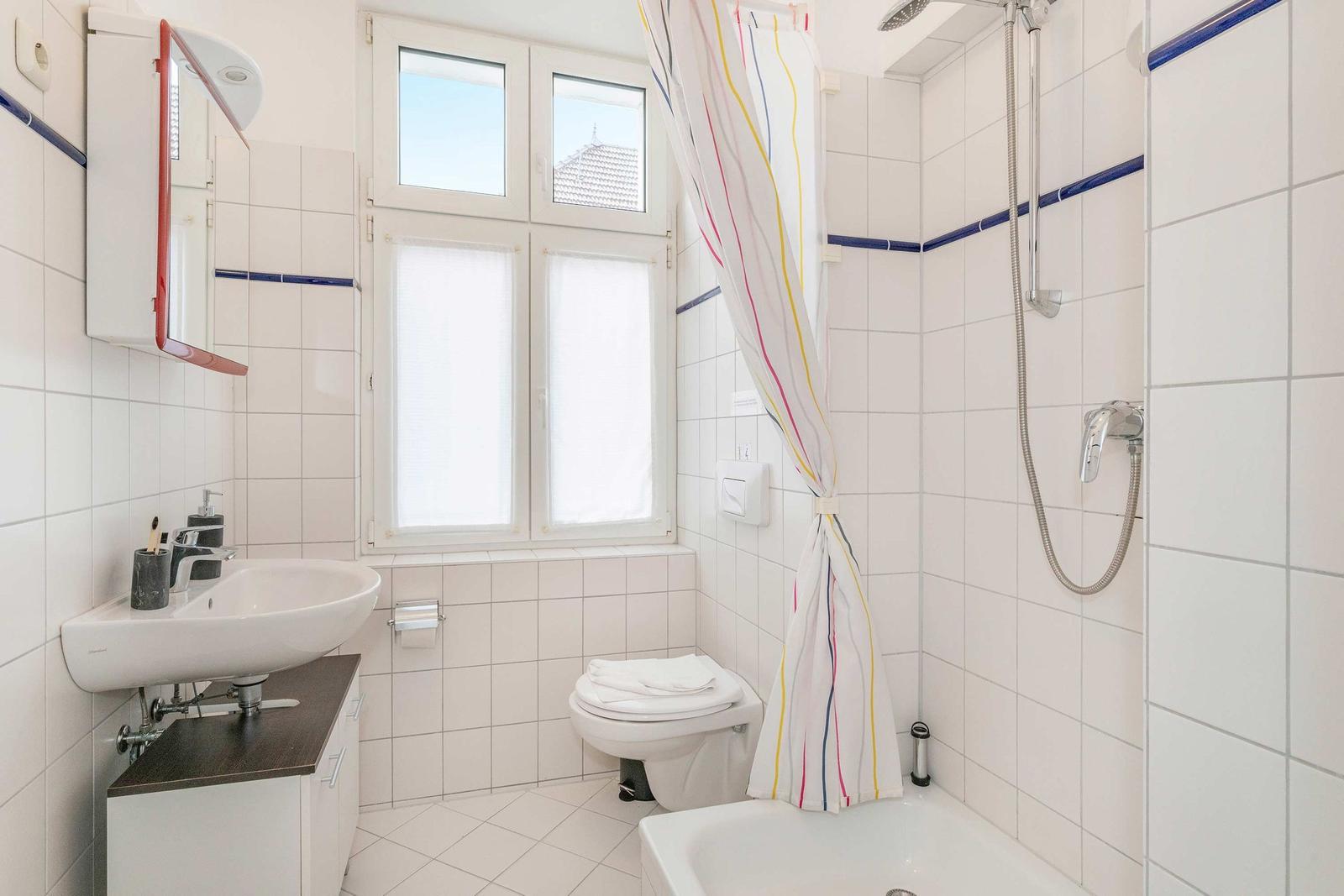 Badezimmer mit Dusche, Toilette und Waschbecken unter Fenster