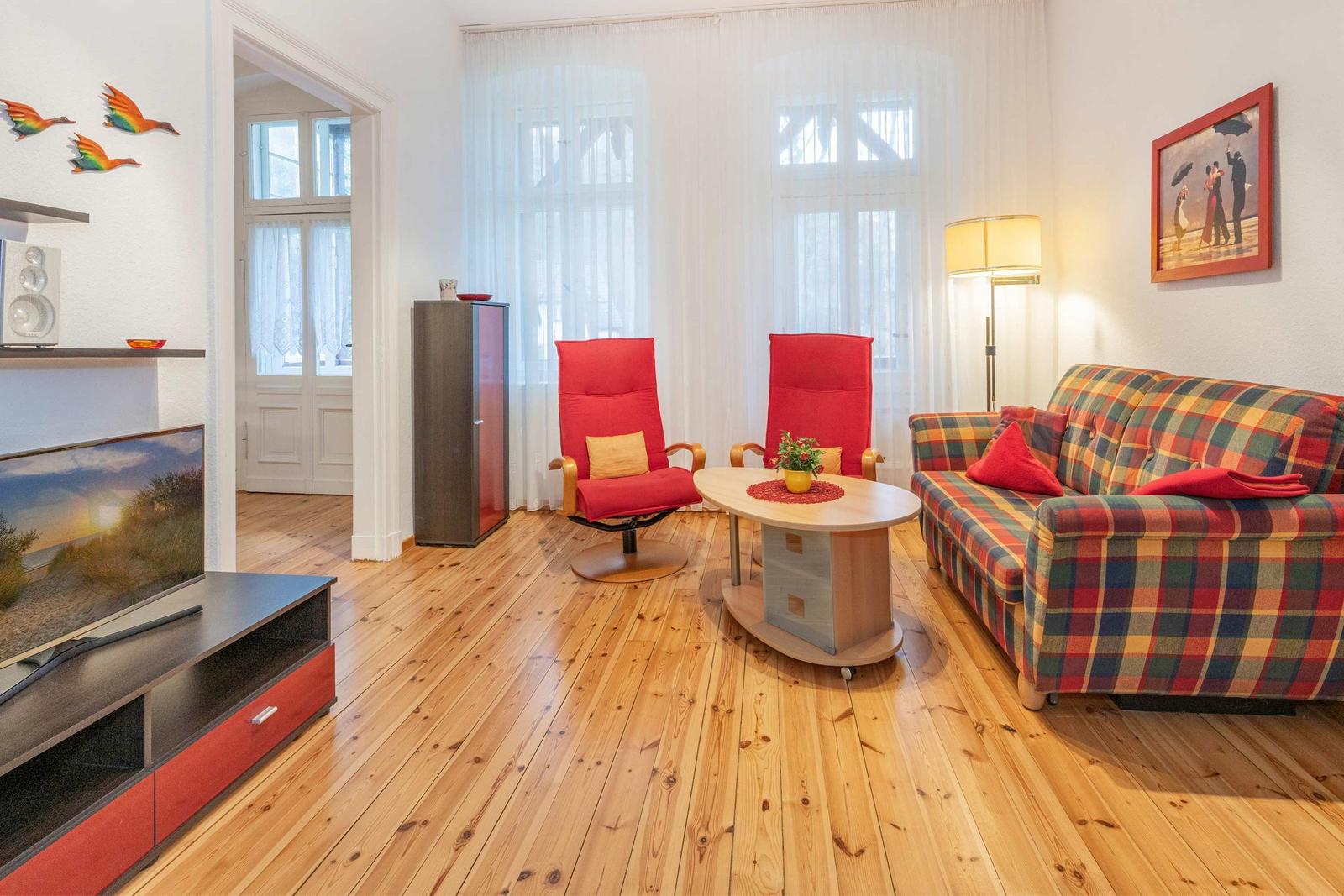 Wohnzimmer mit Holzboden, Sofa, zwei roten Sesseln und Fernseher.